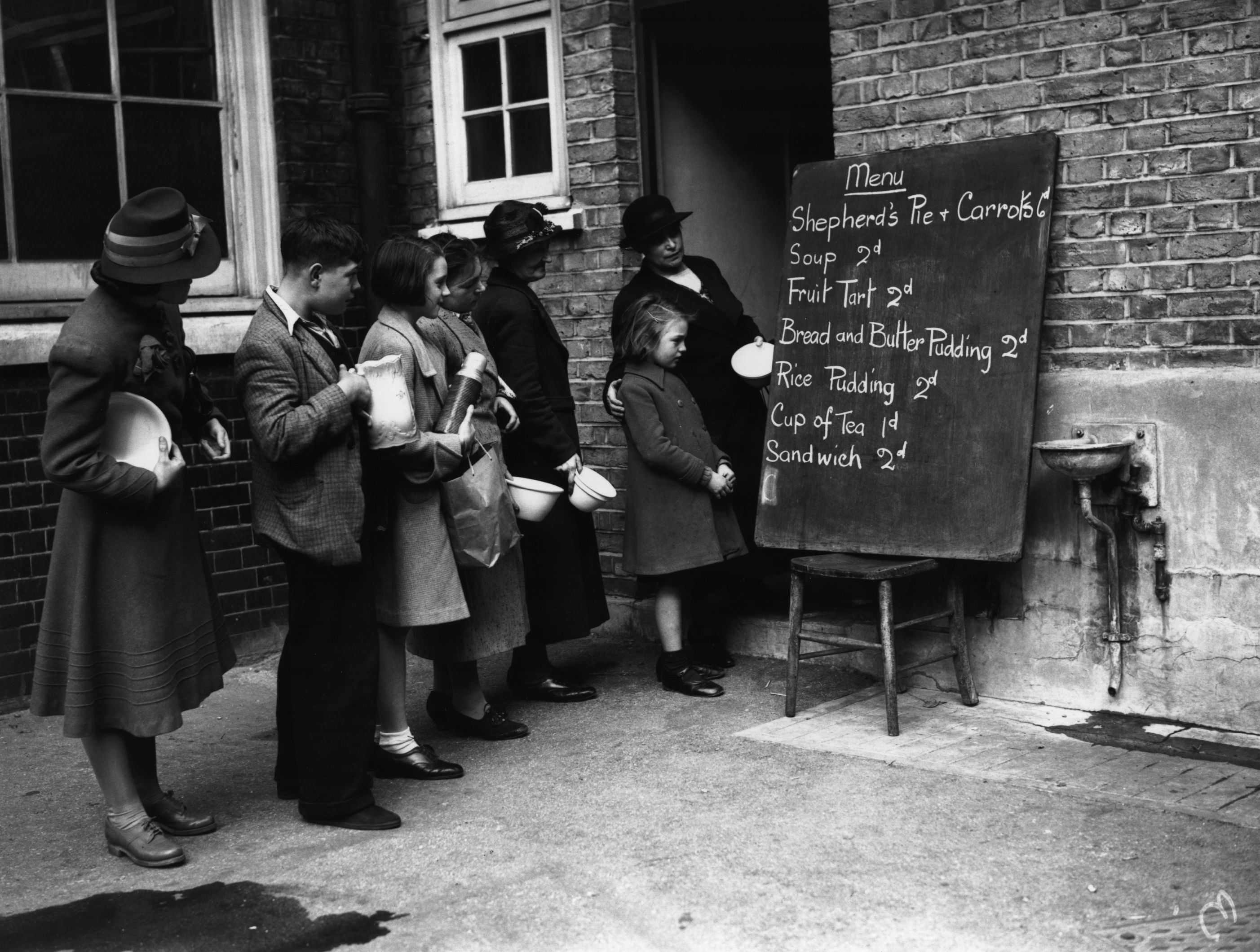 People look at a basic menu while queuing to get into a makeshift canteen in 1940