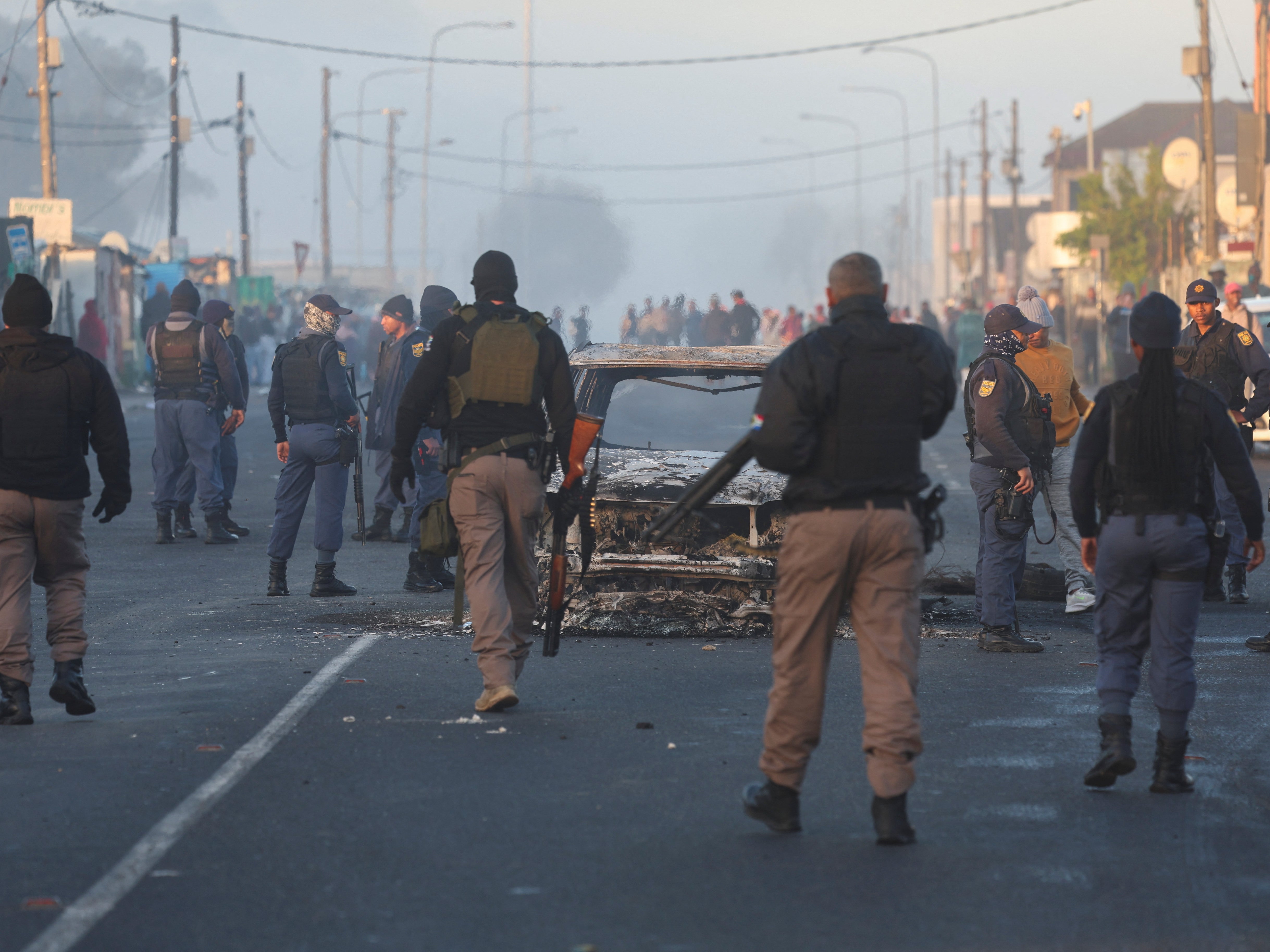 Cape Town law enforcement officials stand around a burnt-out vehicle in Nyanga