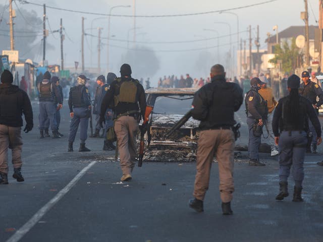 <p>Cape Town law enforcement officials stand around a burnt-out vehicle in Nyanga</p>