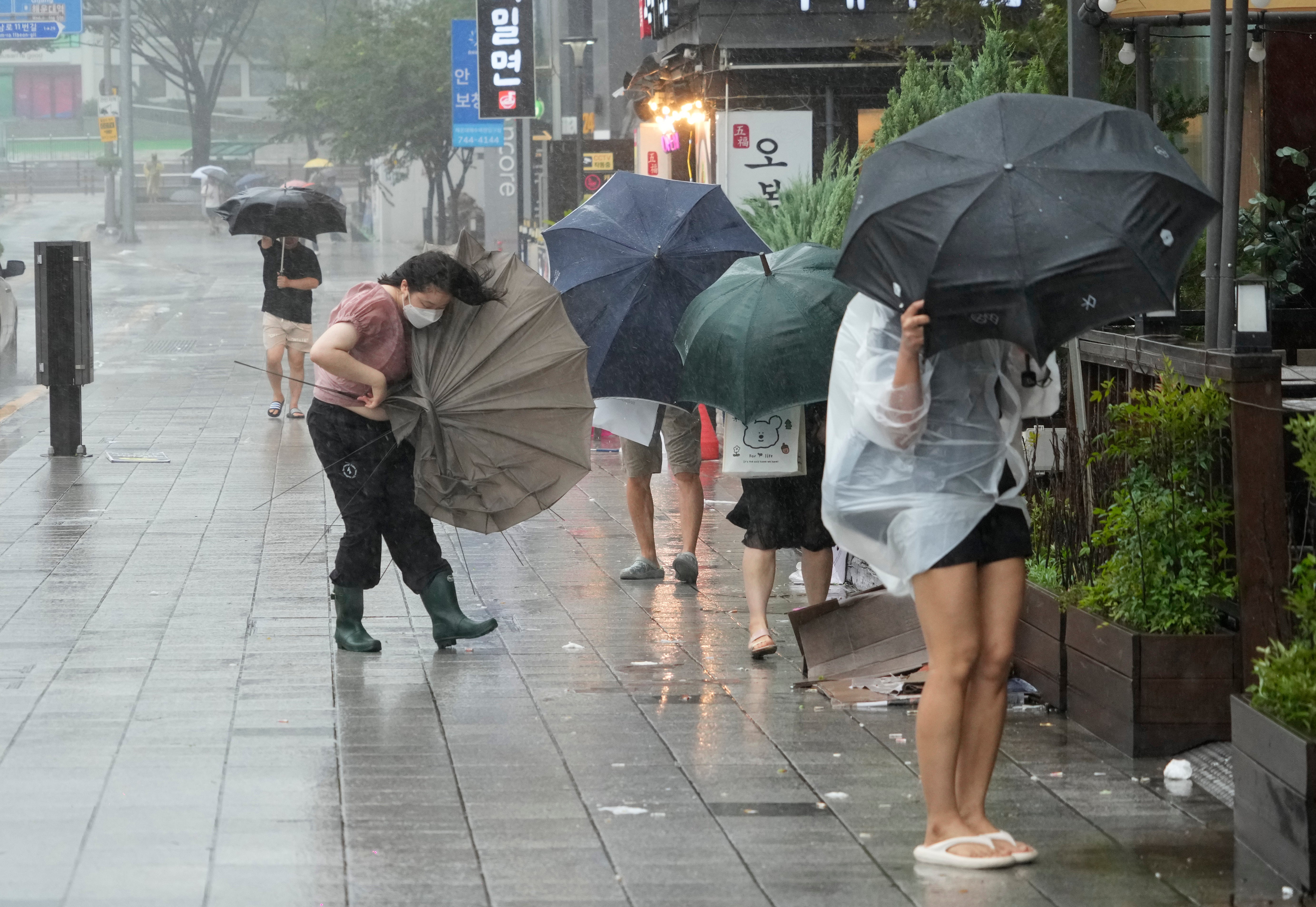 People struggle to hold on to their umbrellas in the rain and wind in Busan, South Korea