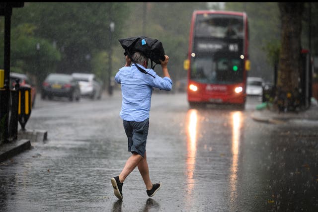 <p>A man uses a bag for shelter as he crosses the road, as torrential rain and thunderstorms hit the country </p>