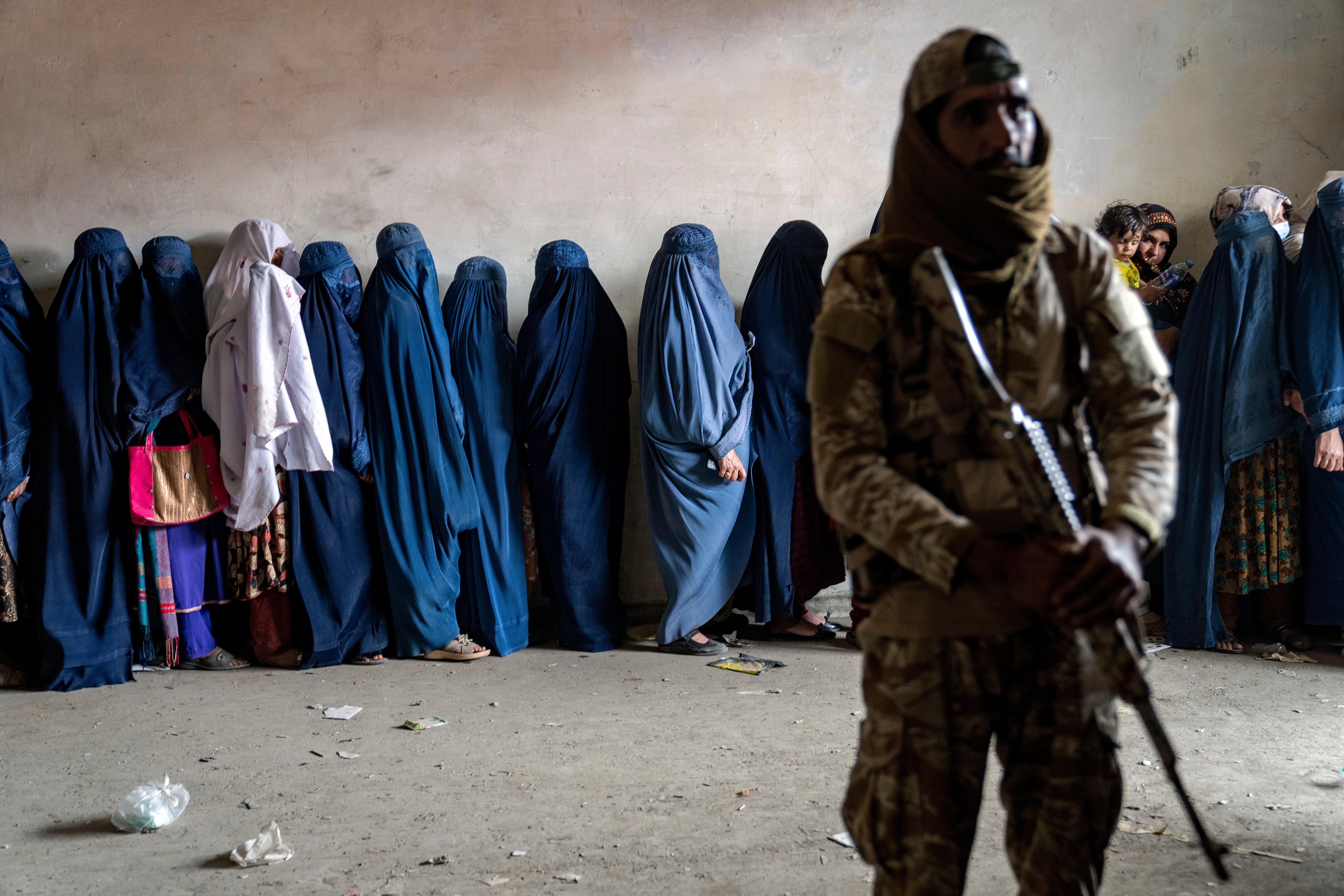 A Taliban fighter stands guard as women wait to receive food rations distributed by a humanitarian aid group in Kabul in May