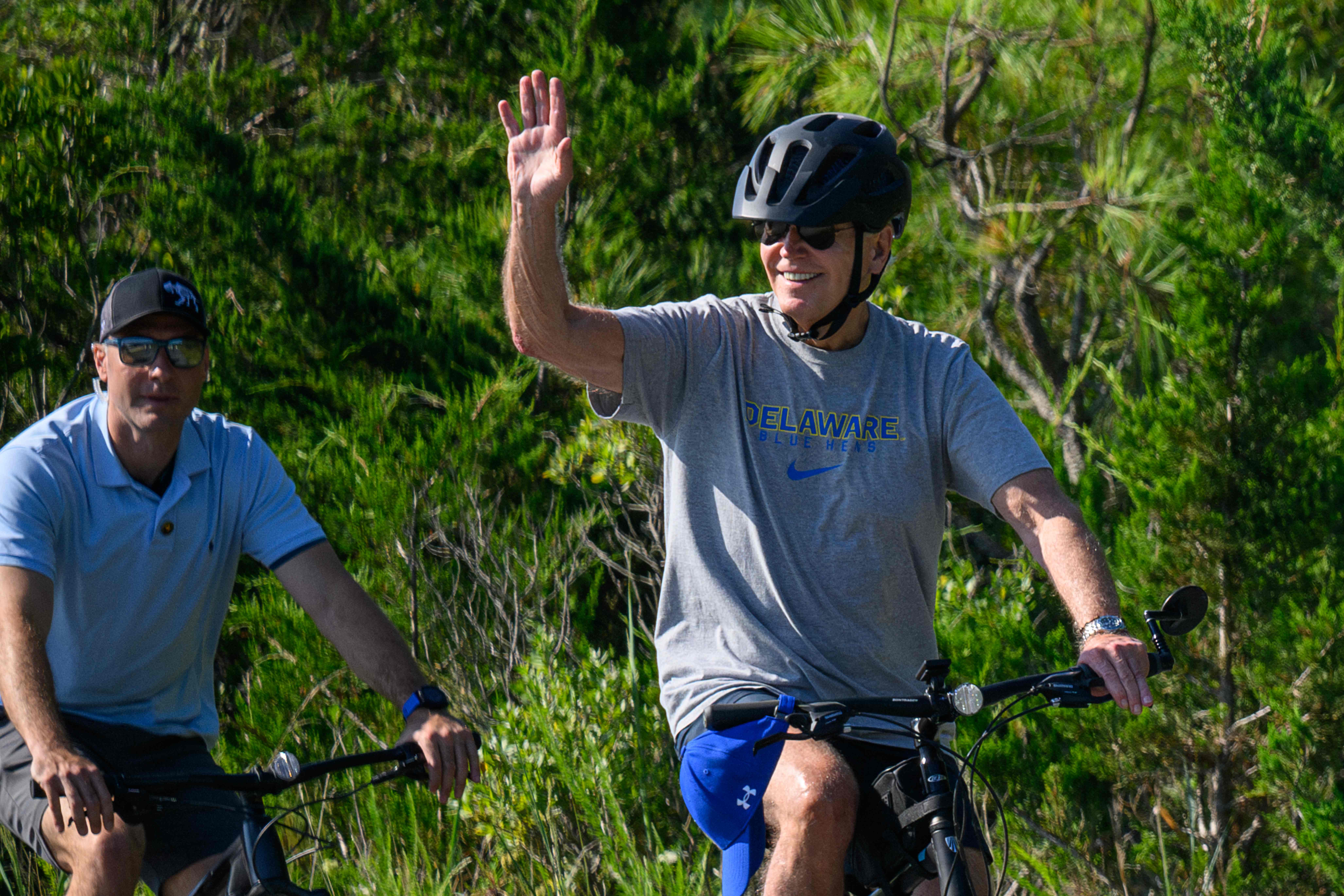Joe Biden waves as he rides his bicycle through Cape Henlopen State Park in Rehoboth Beach on 13 August