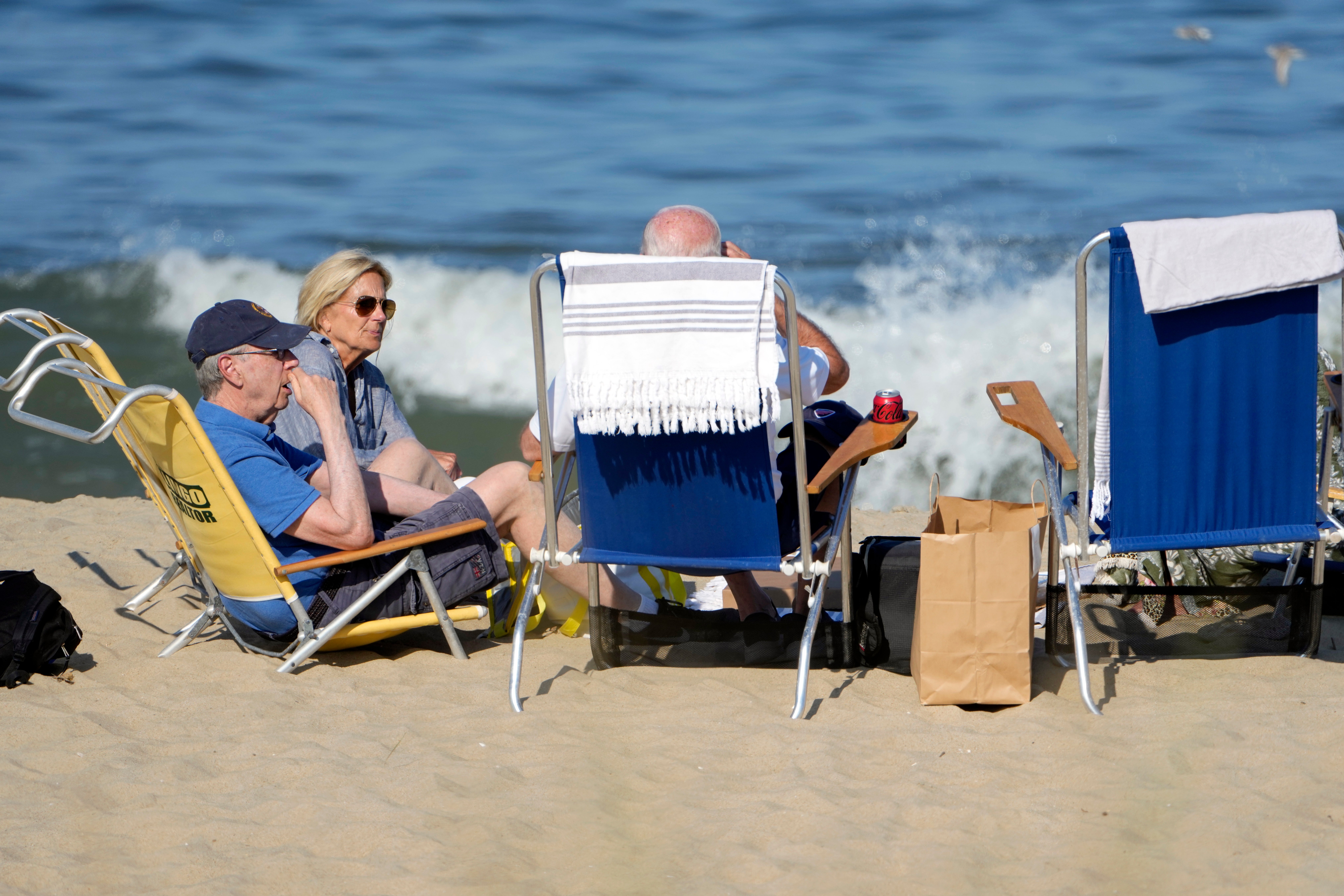 President Joe Biden, back to camera, sits with U.S. Ambassador to the European Union Mark Gitenstein, left, and first lady Jill Biden on the beach near his family home in Rehoboth Beach