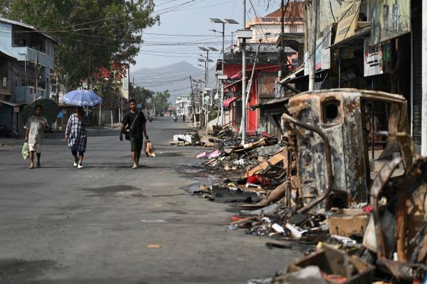 People walk past a burnt vehicle and rubble on a street in Churachandpur in violence hit areas of northeastern Indian state of Manipur on 9 May 2023
