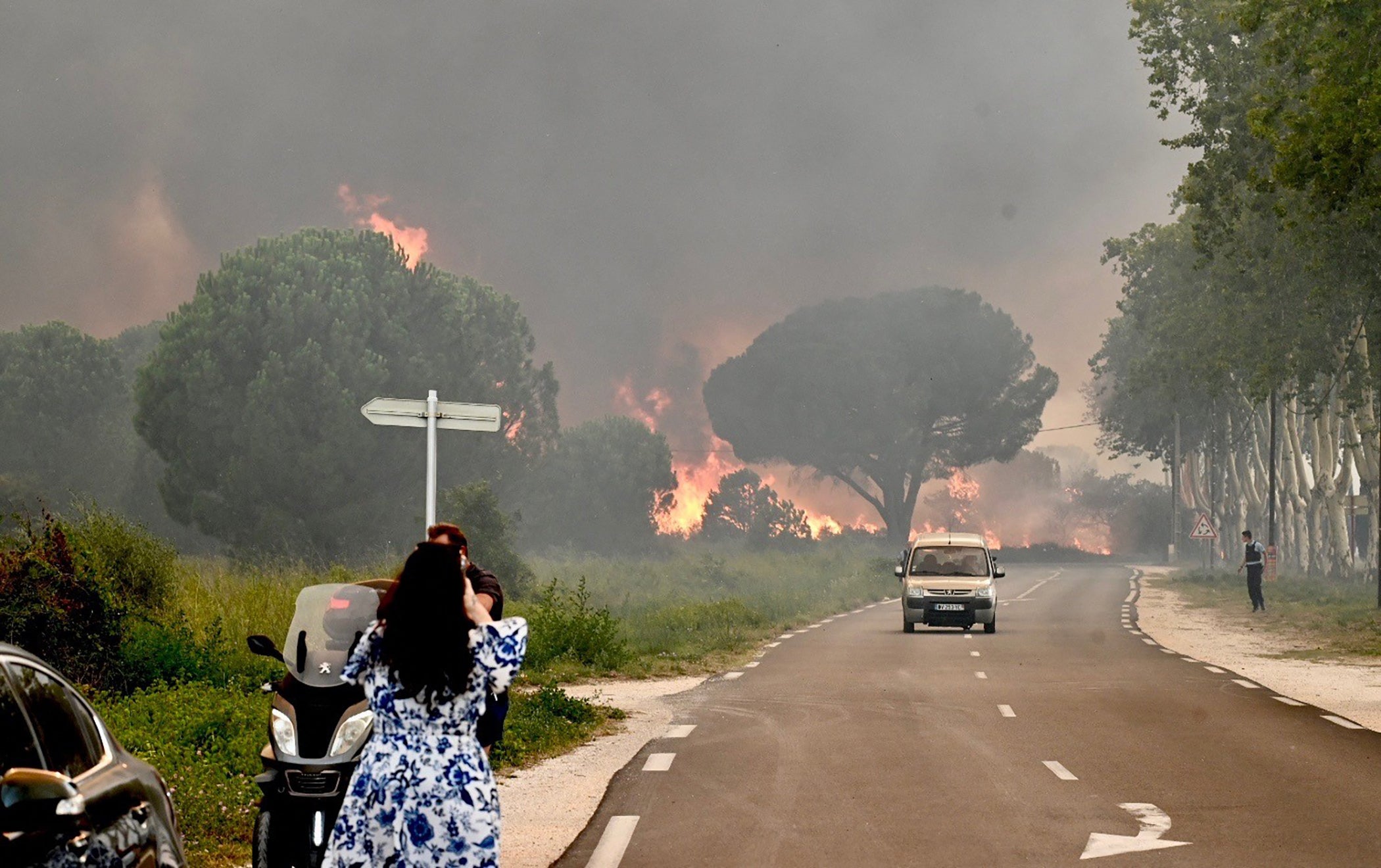 A woman stops at a safe distance to take a picture of the fires, still raging across the department