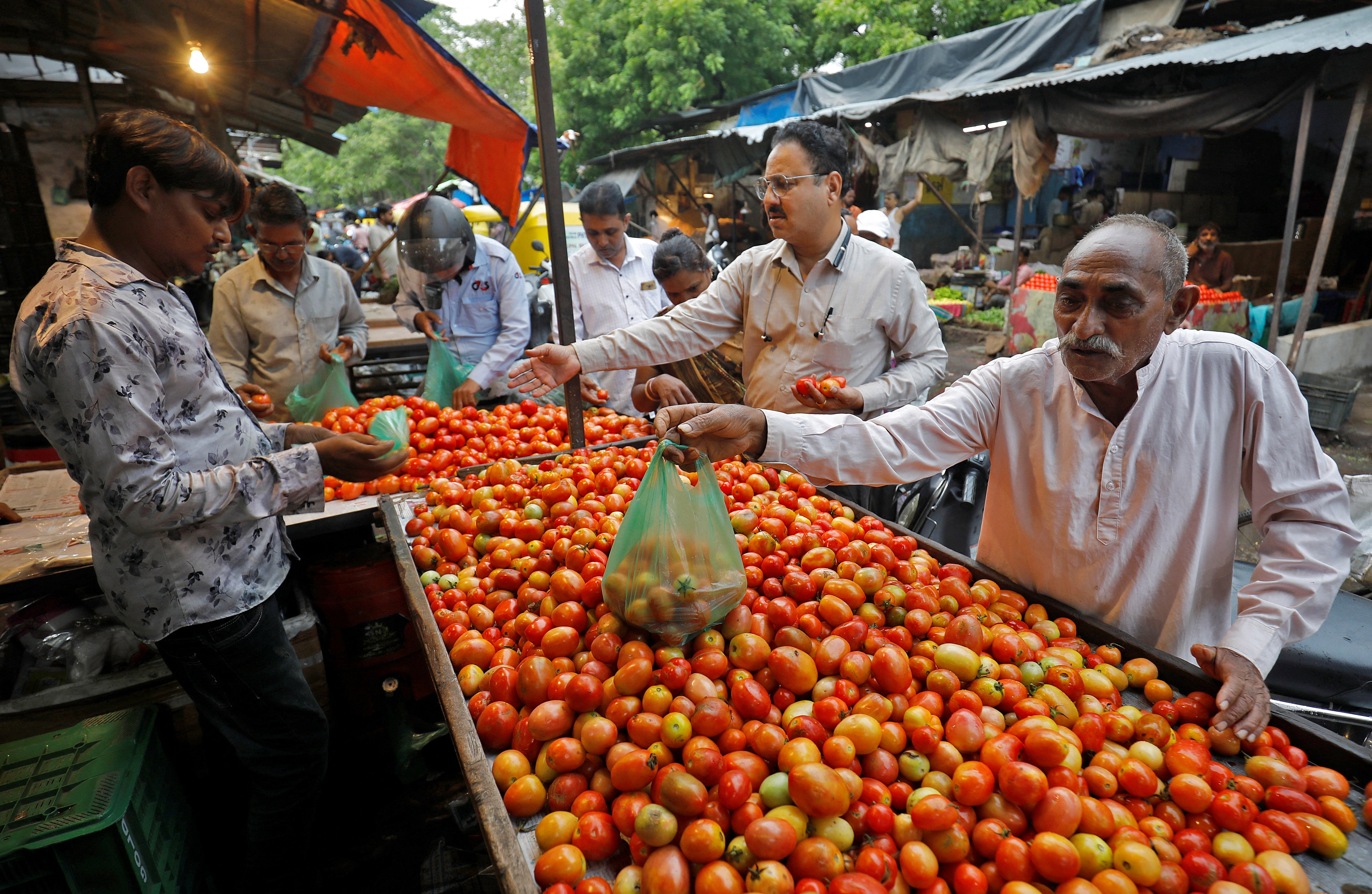 People buy tomatoes from a vendor at a vegetable market in Ahmedabad, India