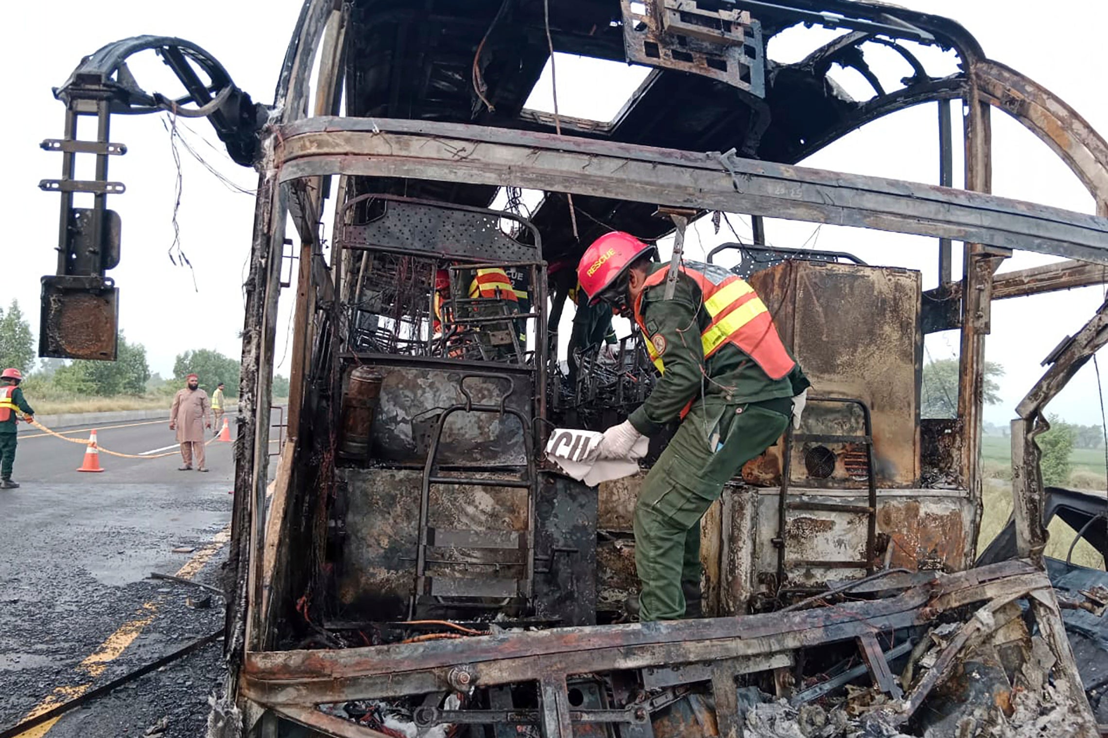 Rescue workers examine a burnt bus at the accident site on a highway in Pindi Bhattian, Pakistan