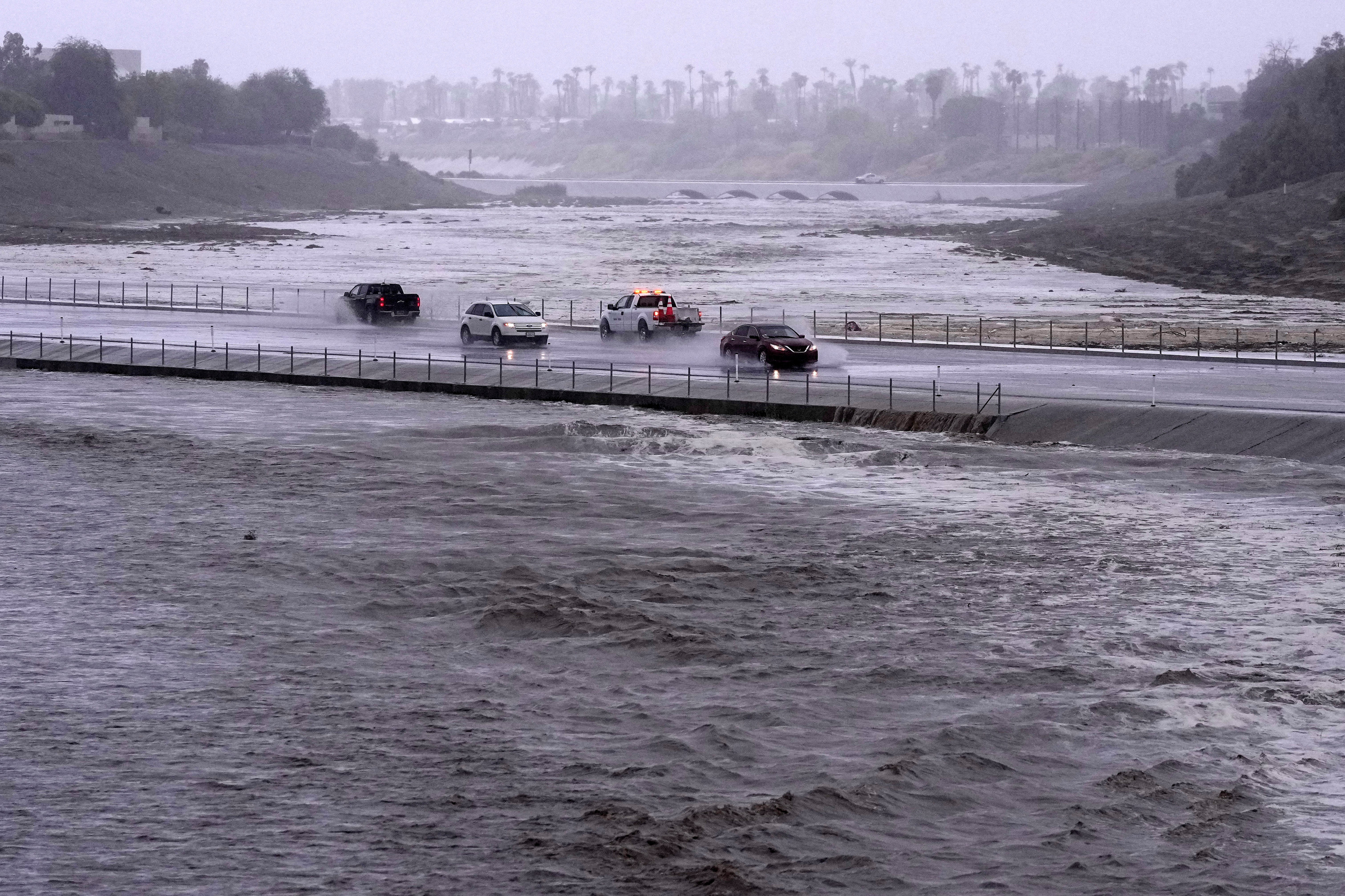 <p>Vehicles cross over a flood control basin that has almost reached the street</p>