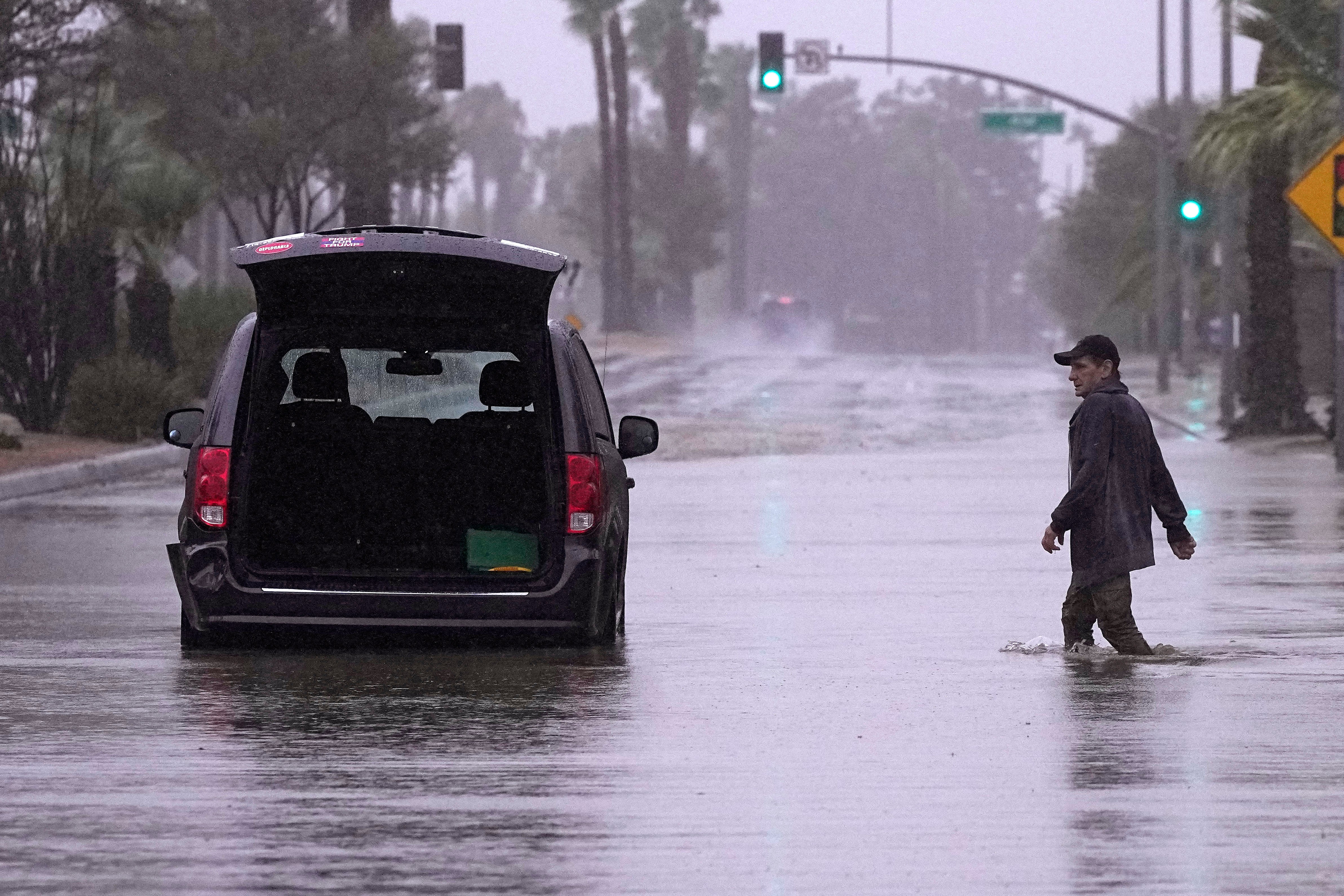 <p>A motorist walks out to remove belongings from his vehicle after becoming stuck in a flooded street</p>