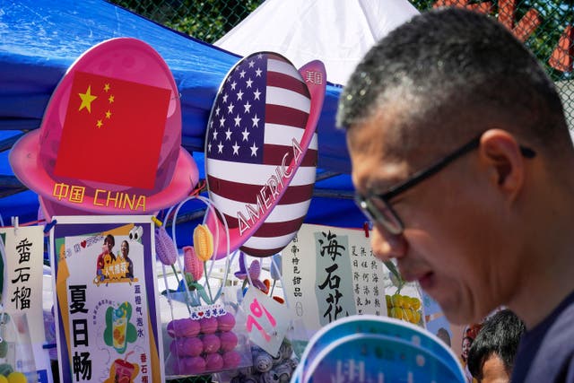 <p>A man walks by a booth selling foods and beverages displaying planet-shaped flags of China and the US in Beijing</p>