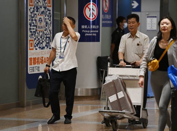 Two North Korean men (L and 2nd R) walk through the arrivals section at Beijing Capital Airport after the arrival of Air Koryo flight JS151 on 22 August 2023