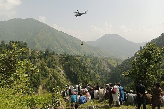 <p>People watch as an army soldier slings down from a helicopter during a mission to rescue those trapped in the cable car</p>