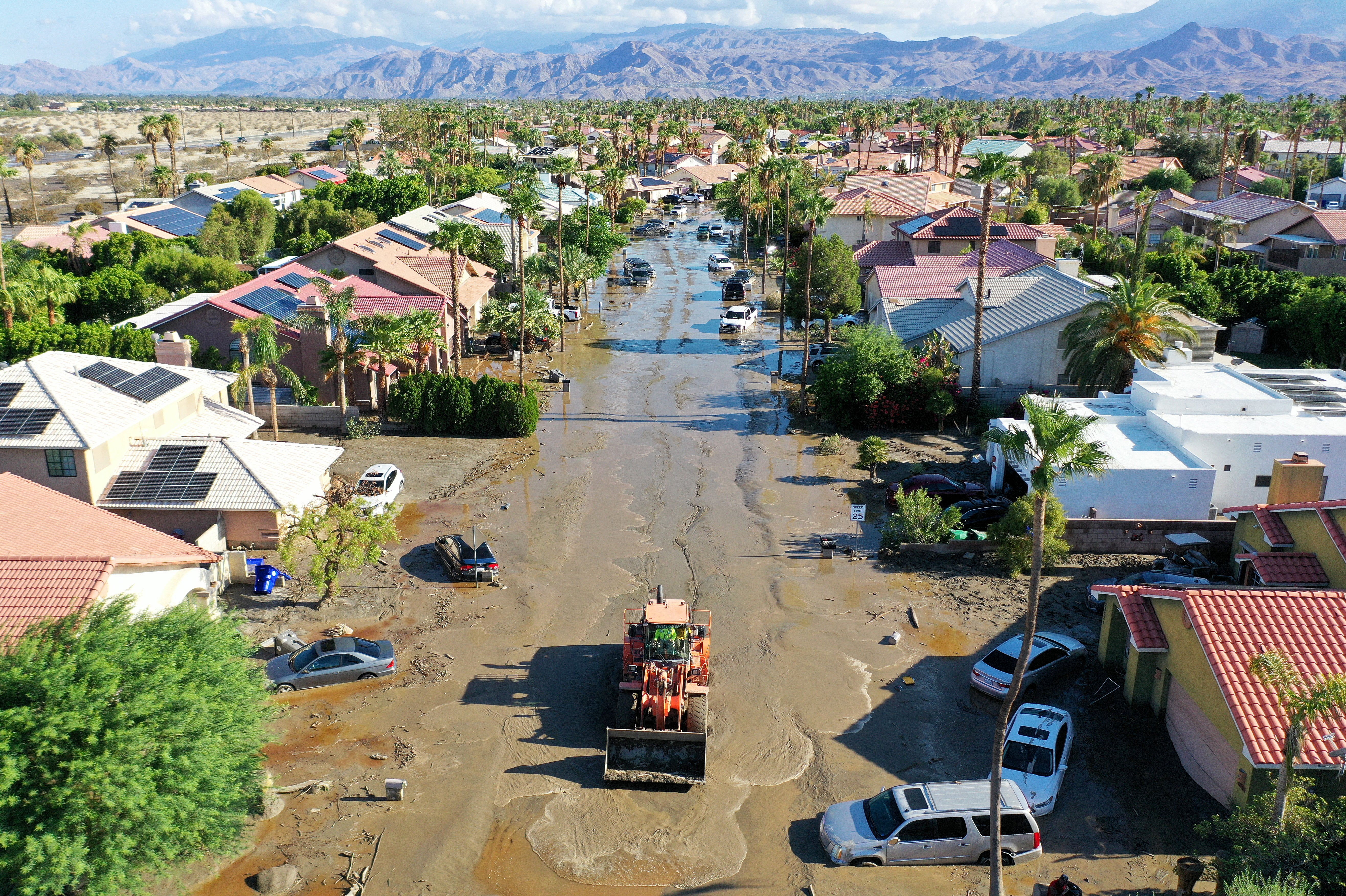 An aerial view of a maintenance vehicle clearing mud near stranded vehicles along a flooded street after Tropical Storm Hilary floodwaters inundated an area of Cathedral City, California
