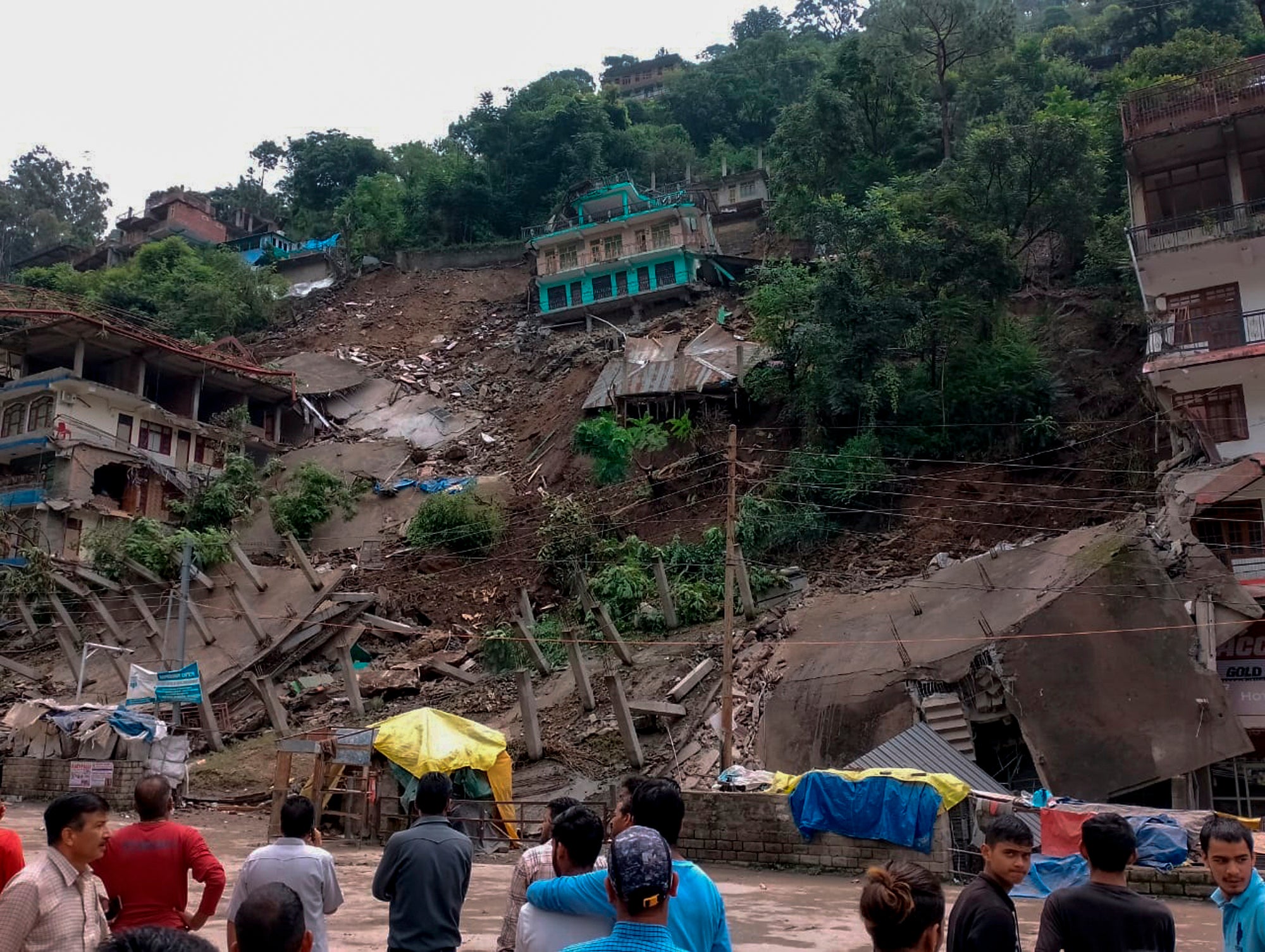 People look on after several buildings that had recently developed cracks and were evacuated, collapsed following heavy rains in Anni