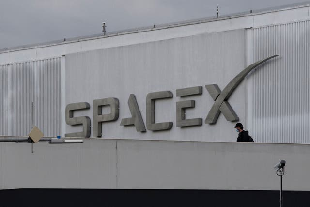 <p>A pedestrian wears a face mask while crossing a bridge from the Space Exploration Technologies Corp. (SpaceX) headquarters on January 28, 2021 in Hawthorne, California</p>