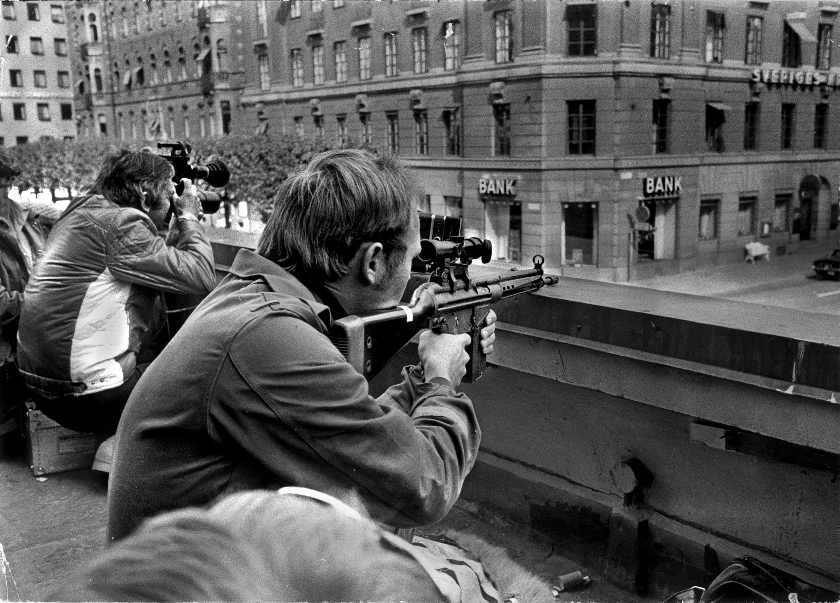 Press photographers and police snipers crouch side-by-side on a roof opposite the Kreditbanken