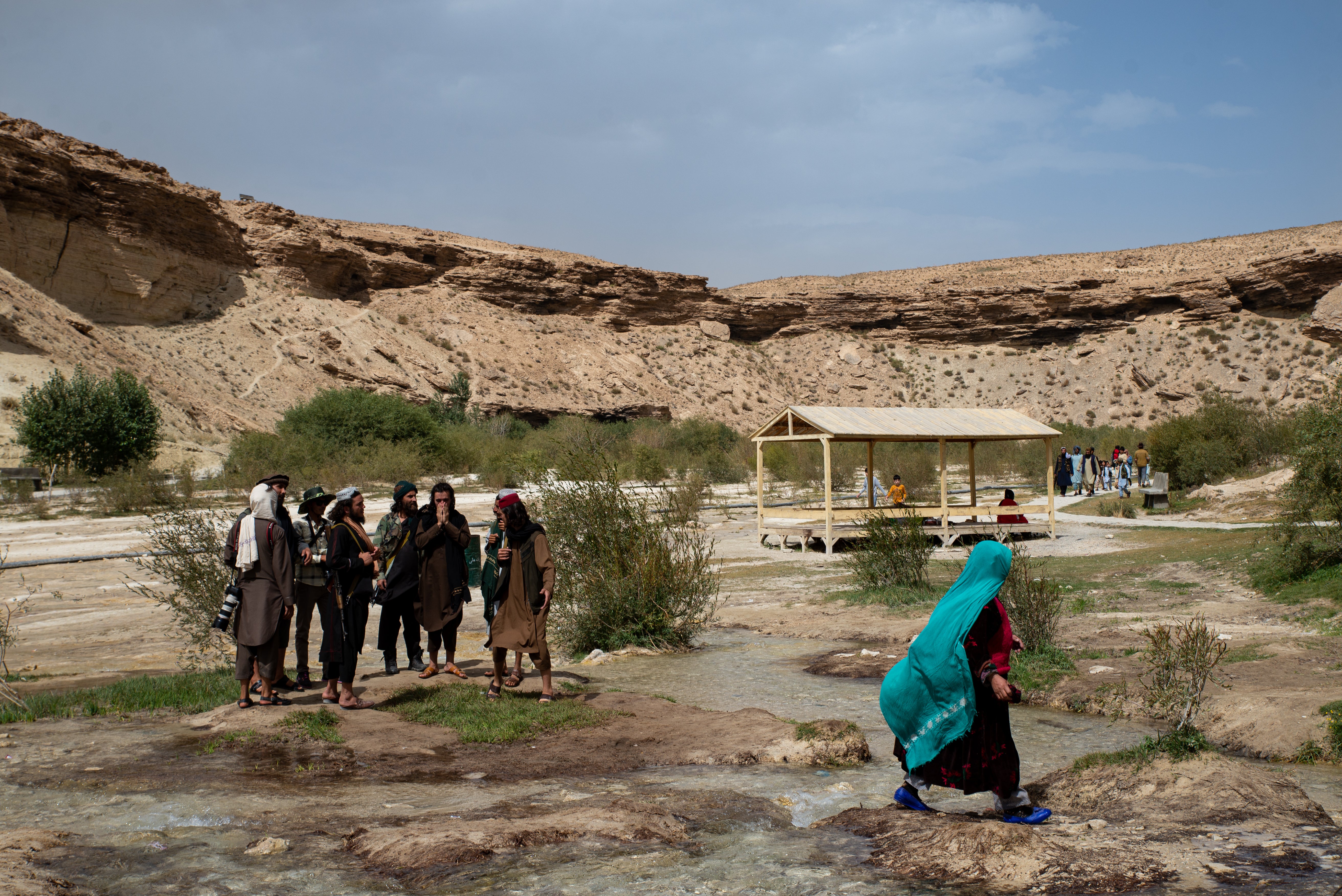 An Afghan woman walks past Taliban members at Band-e Amir National Park, a popular weekend destination, in Band-e Amir, central Afghanistan