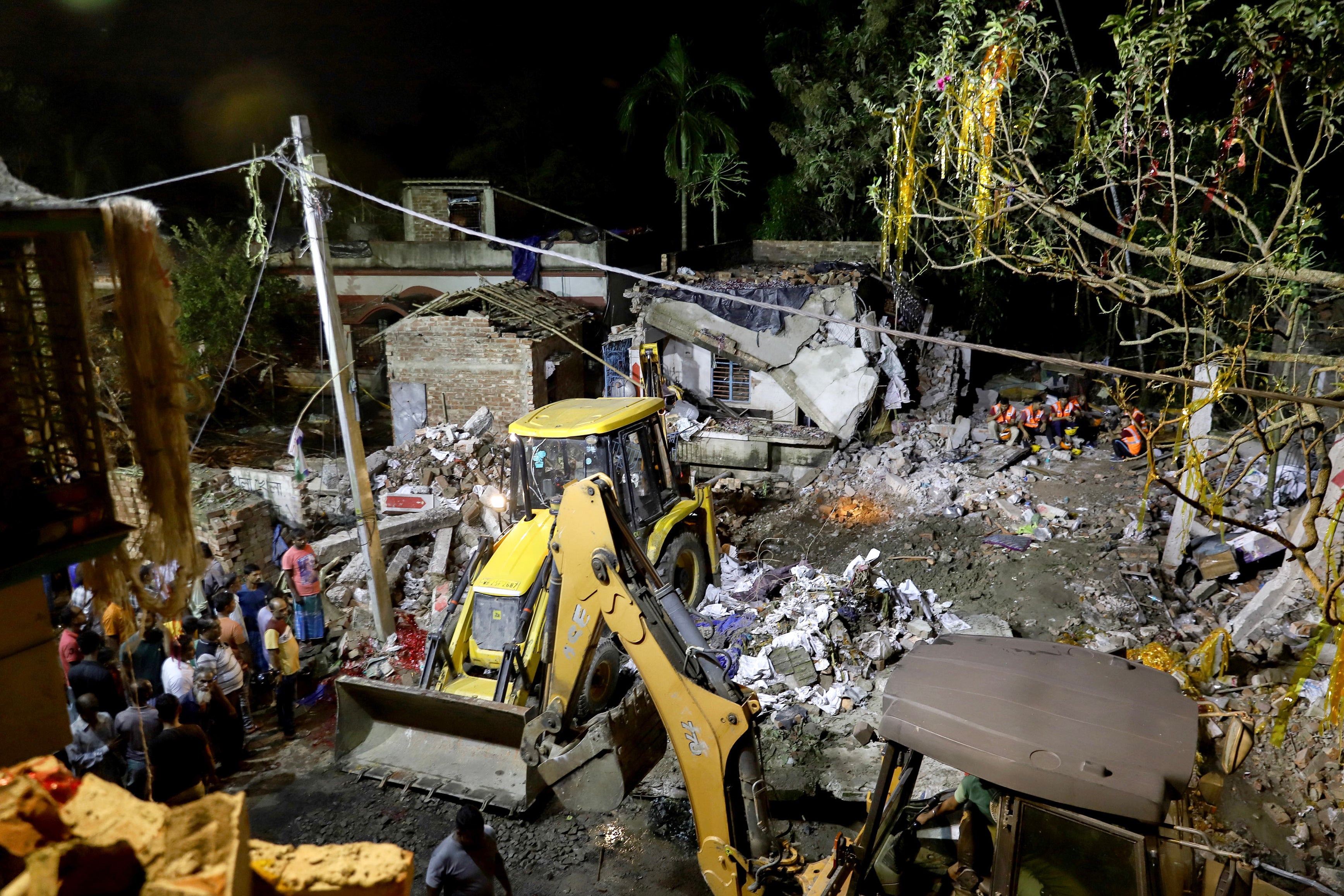 Locals gather at the scene as emergency workers search the debris after a massive explosion occurred at a firecracker factory