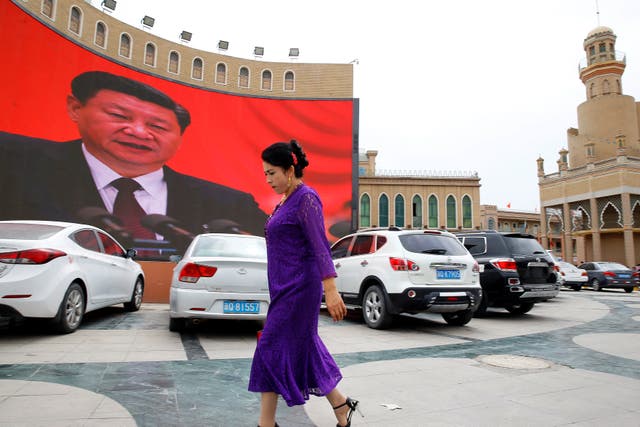 <p>An ethnic Uighur woman walks in front of a giant screen with a picture of Chinese President Xi Jinping</p>