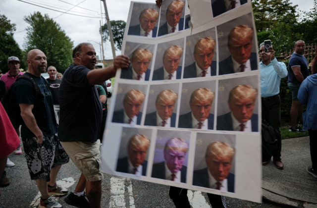 <p>A protester holds up images of Donald Trump’s Georgia mug shot </p>