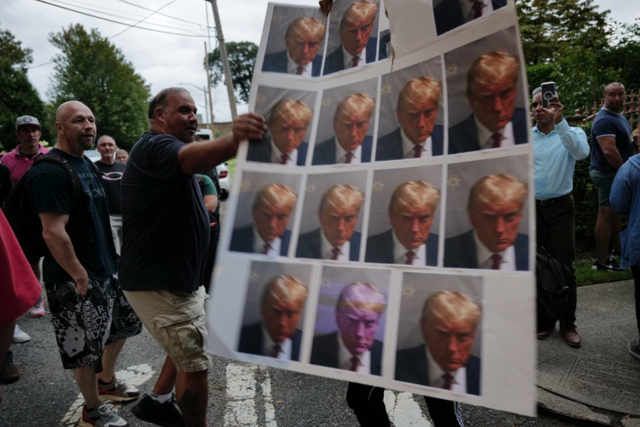 <p>A protester holds up images of Donald Trump’s Georgia mug shot </p>