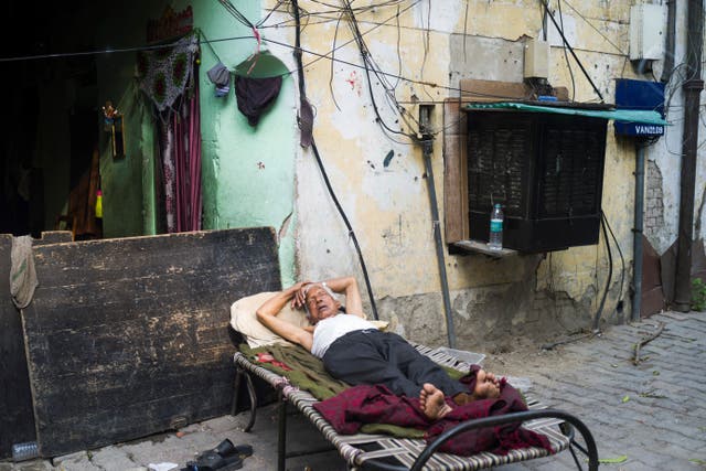 <p>An elderly man sleeps on a cot next to a street outside his home in New Delhi on 17 September 2019</p>