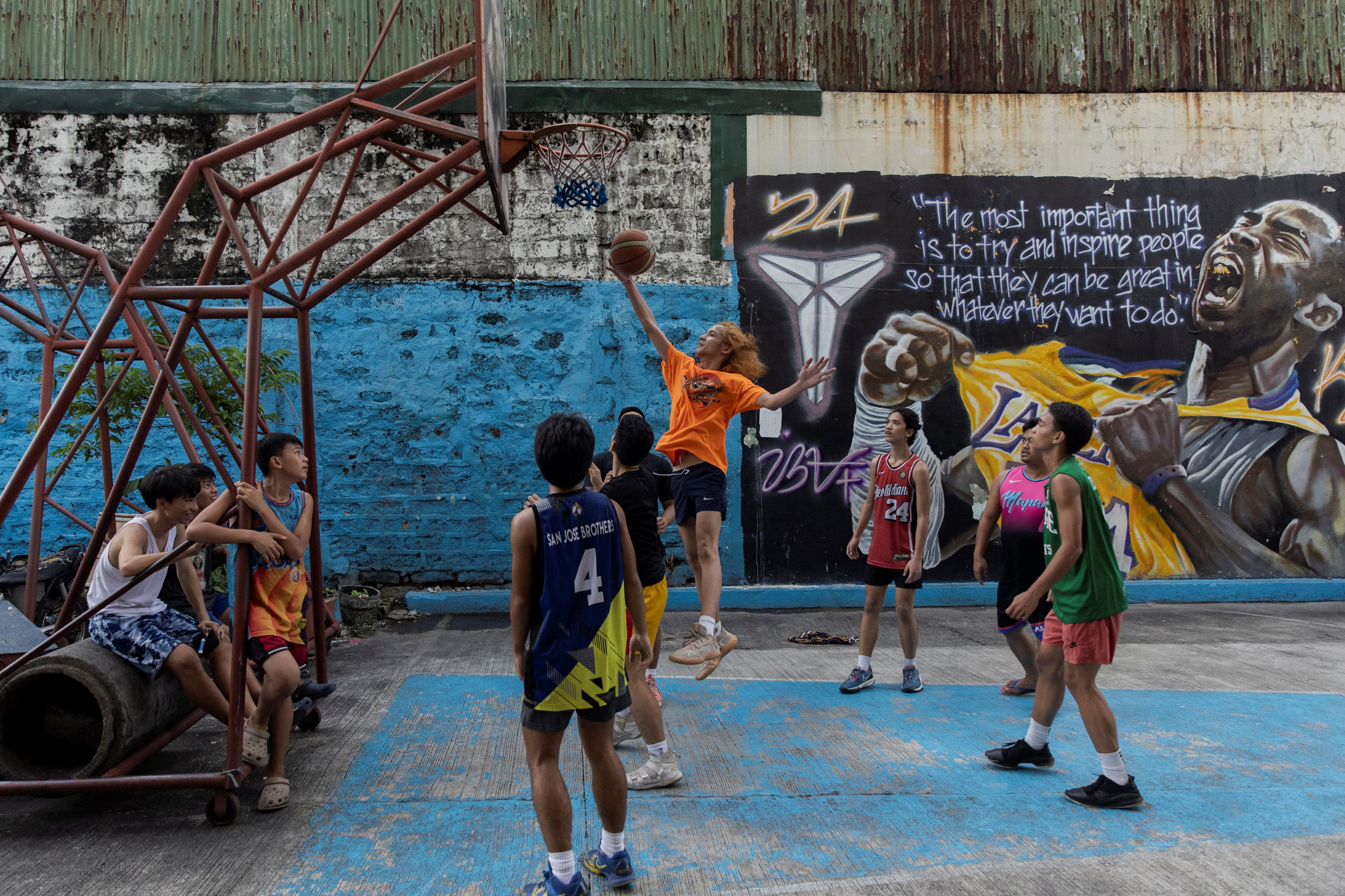 Teenagers play basketball at a court in front of a mural of Kobe Bryant in Manila