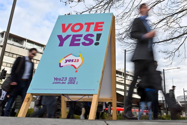 <p>Commuters walk past a vote ‘yes’ stand for the upcoming Voice referendum at the Civic Bus Interchange in Canberra on 30 August </p>