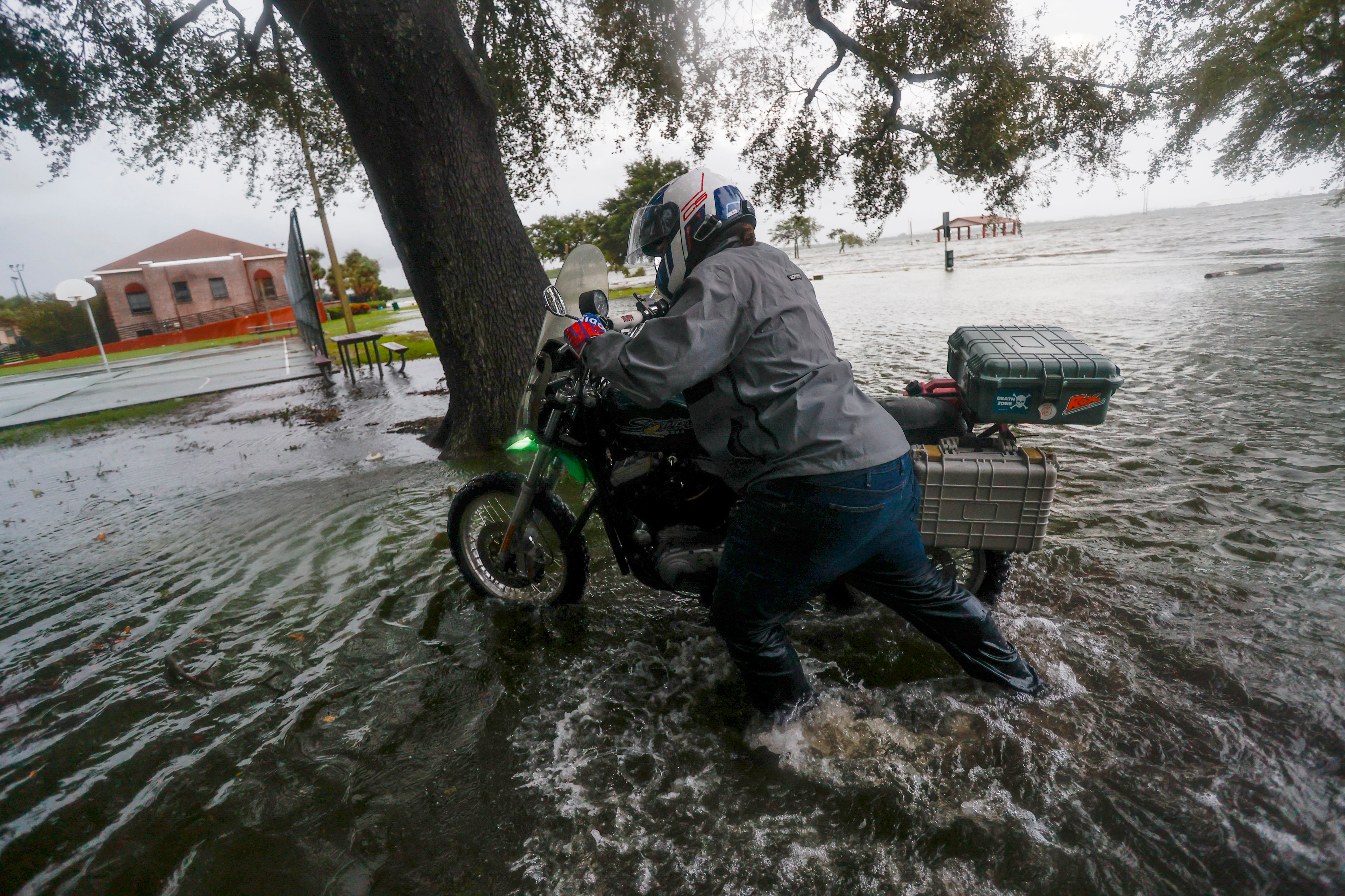 A man walks his motorcycle to Desoto Park after attempting to ride through an impassable South Bermuda Boulevard at Palmetto Beach