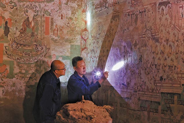 <p>Li Bo (right), a veteran restorer of the Dunhuang Academy, leads a colleague in examining murals in one of the Yulin Caves at Guazhou county near Dunhuang, Gansu province </p>