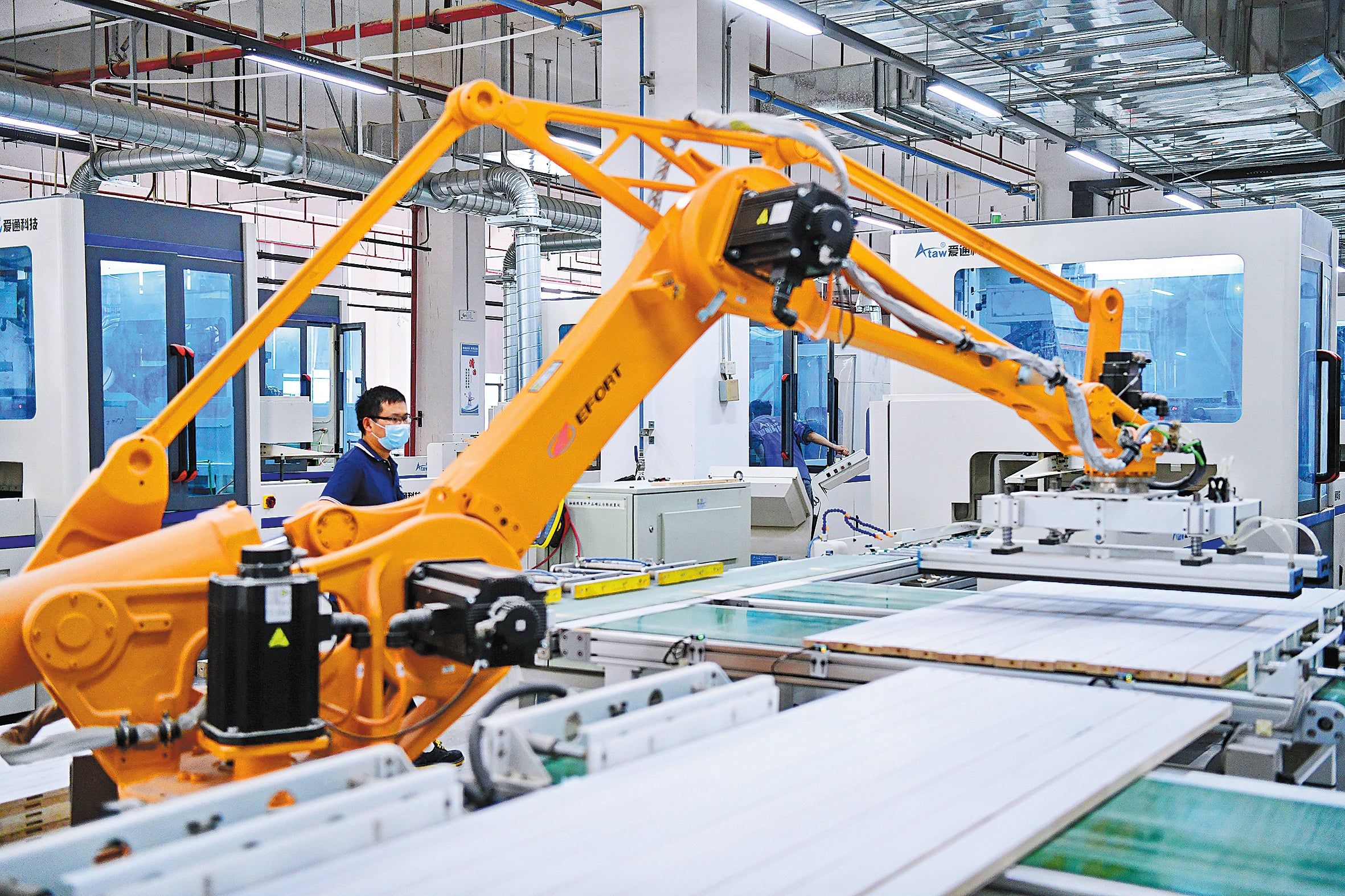 An employee oversees a smart robot processing furniture parts at a production facility in Ganzhou, Jiangxi province, in May, 2023