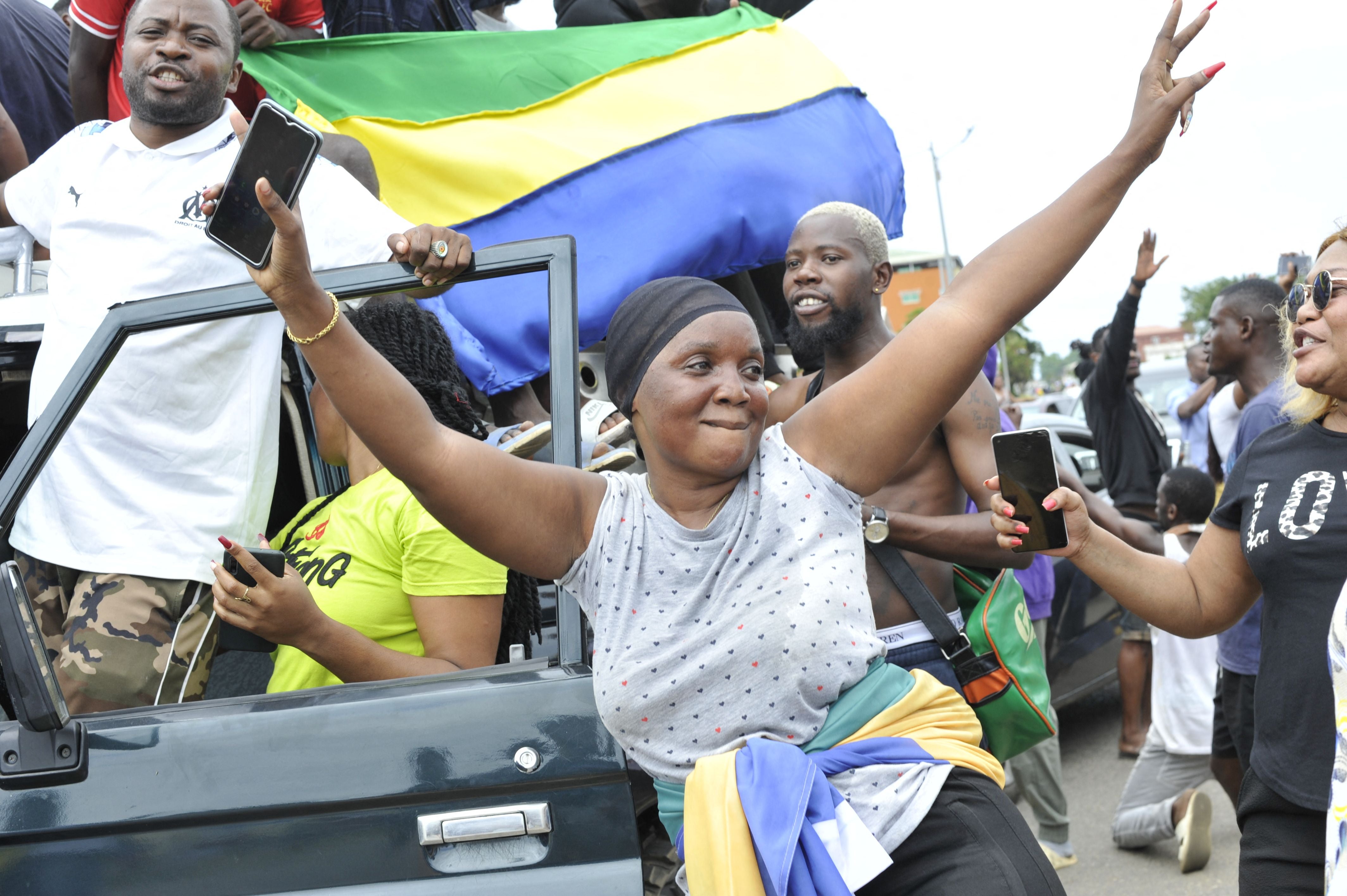 Residents gesture and hold a Gabon national flag as they celebrate in Libreville