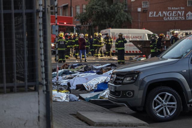 <p>Bodies covered in blankets and sheets are seen at the scene of a fire in Johannesburg on 31 August 2023</p>