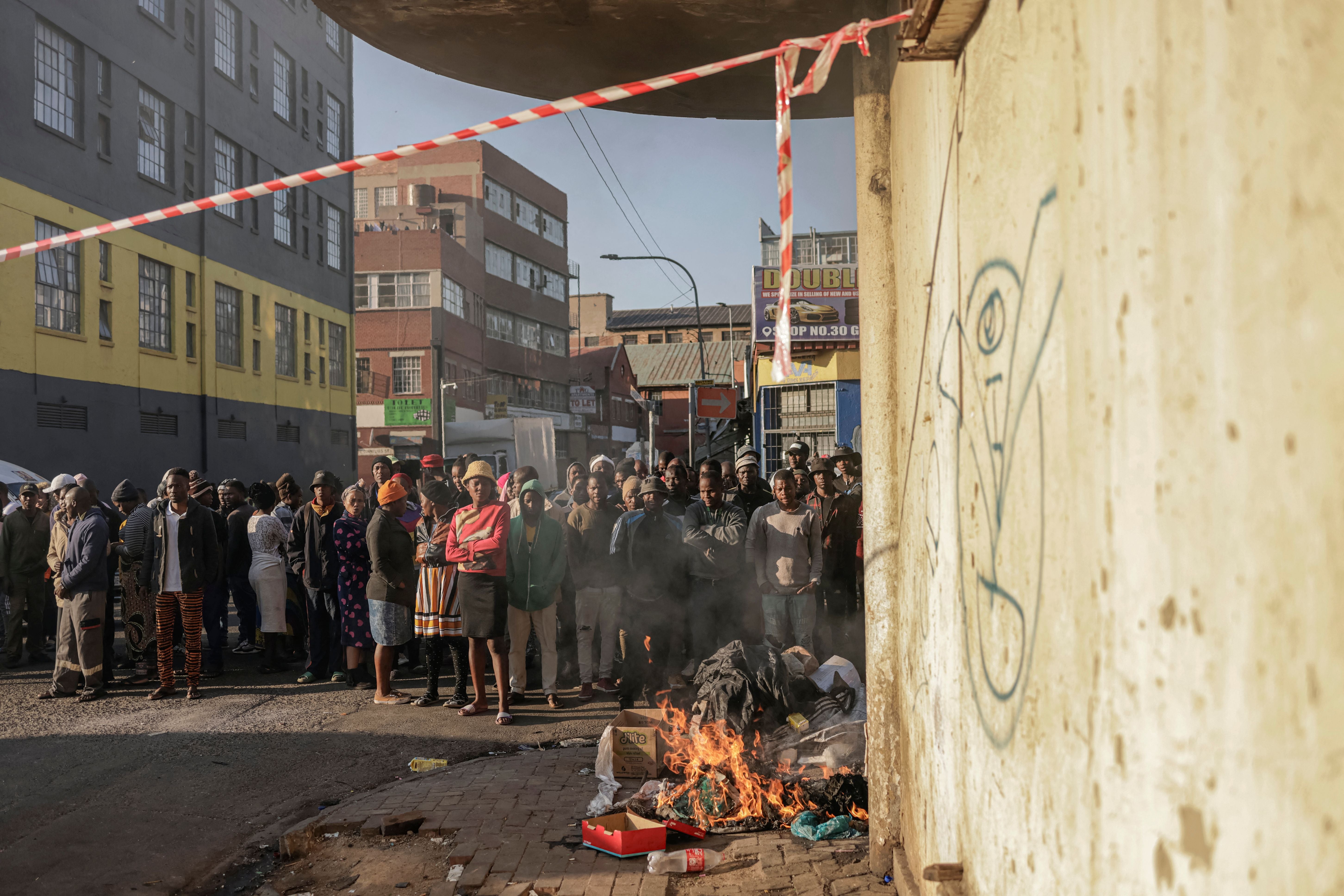 <p> People standing at a bonfire look on as unseen firefighters work at the scene of a fire in a building in Johannesburg on 31 August. </p>