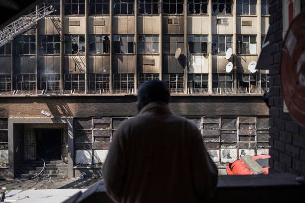 <p>A man looks on at a burned apartment block in Johannesburg on 31 August 2023</p>