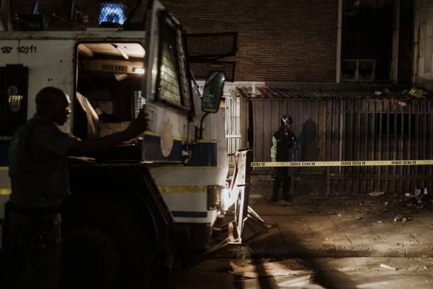 <p>An officer of the South African Police Service (SAPS) climbs on an armoured personnel carrier as a private security guard stands near the entrance of a burned apartment block in Johannesburg on 31 August 2023</p>