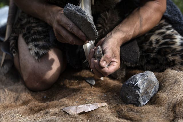 <p>Guido Camia dressed as a Neanderthal Cave man works on a flint ax in a wood near Chianale, in the Italian Alps, near the French border, on 7 August 2019</p>