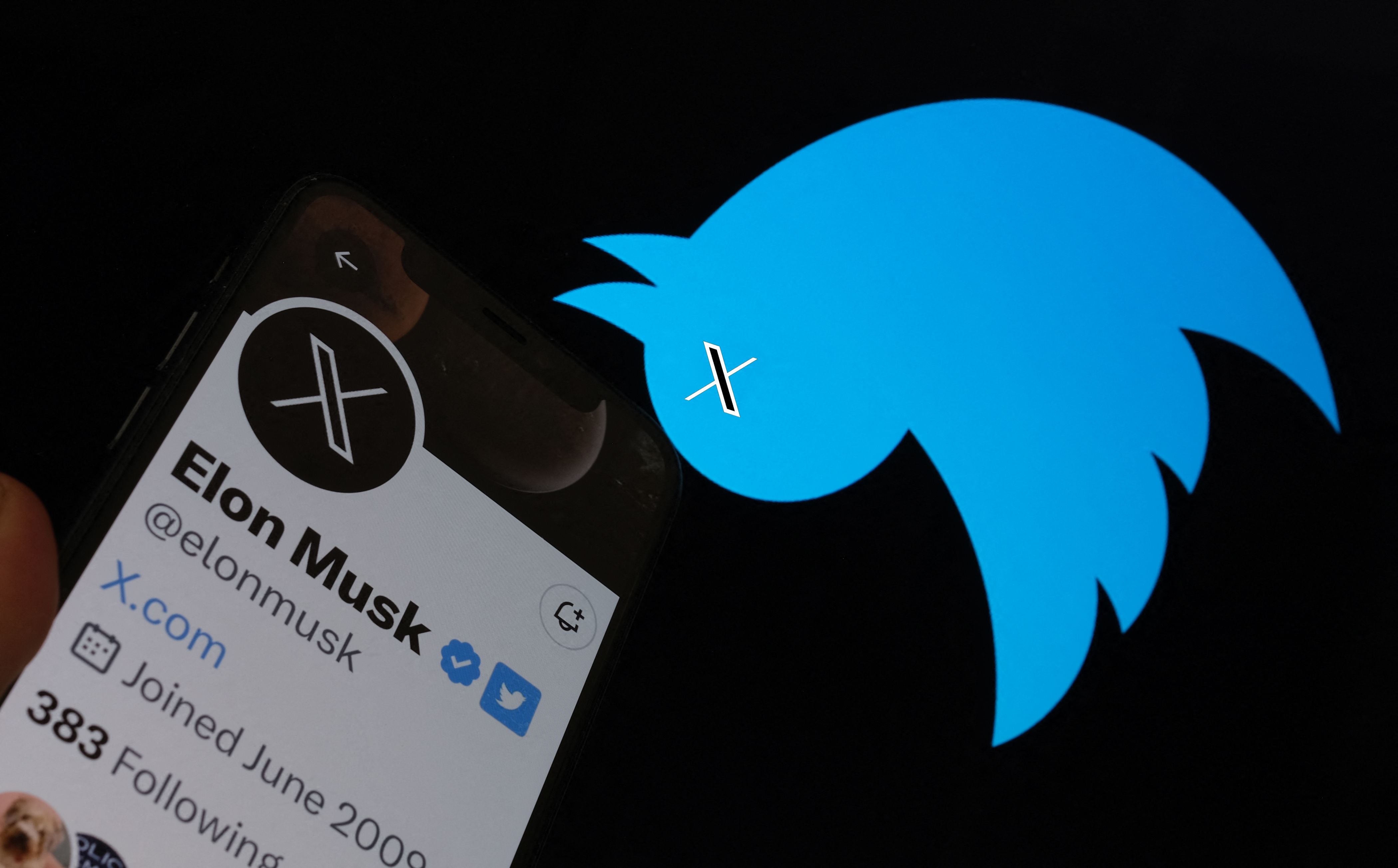 This illustration photo taken on 24 July 2023 shows the Twitter bird logo upside down in the background of Elon Musk’s screen advertising an ‘X’ as a replacement logo