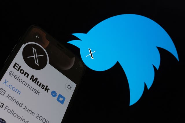 <p>This illustration photo taken on 24 July 2023 shows the Twitter bird logo upside down in the background of Elon Musk’s screen advertising an ‘X’ as a replacement logo</p>