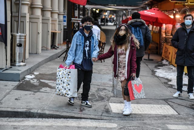 <p>A couple hold hands as they cross the street carrying gift bags on Valentine’s Day on February 14, 2021 in the Soho neighborhood in New York City</p>