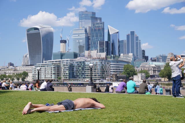 People enjoy the hot weather with a view of the city of London skyline. London stocks finished higher on Tuesday (Lucy North/PA)