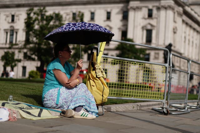 A woman shelters from the sun under an umbrella in Parliament Square, London (Jordan Pettitt/PA)