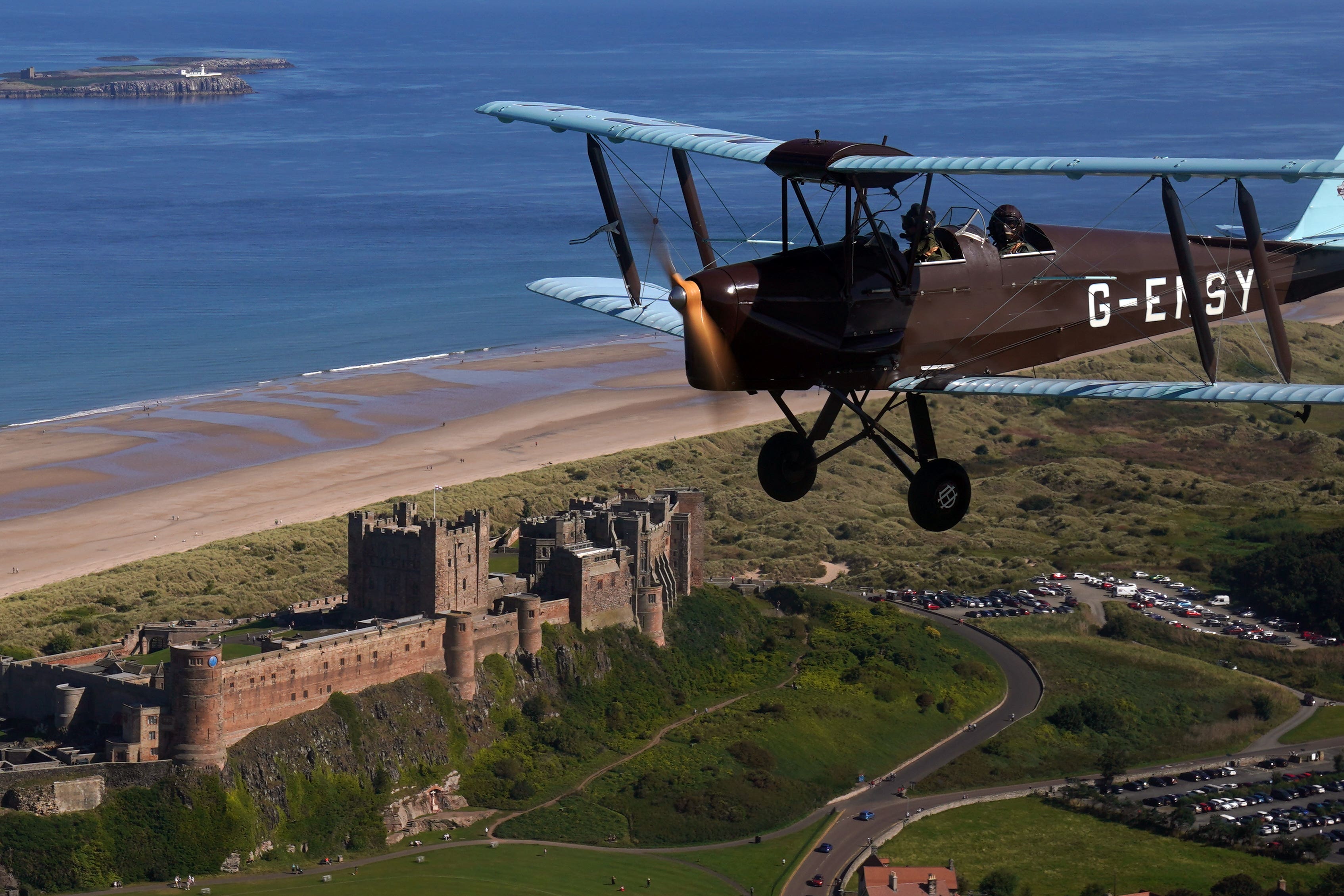 The Second World War vintage Tiger Moth plane takes to the sky over Bamburgh Castle in Northumberland (Owen Humphreys/PA)