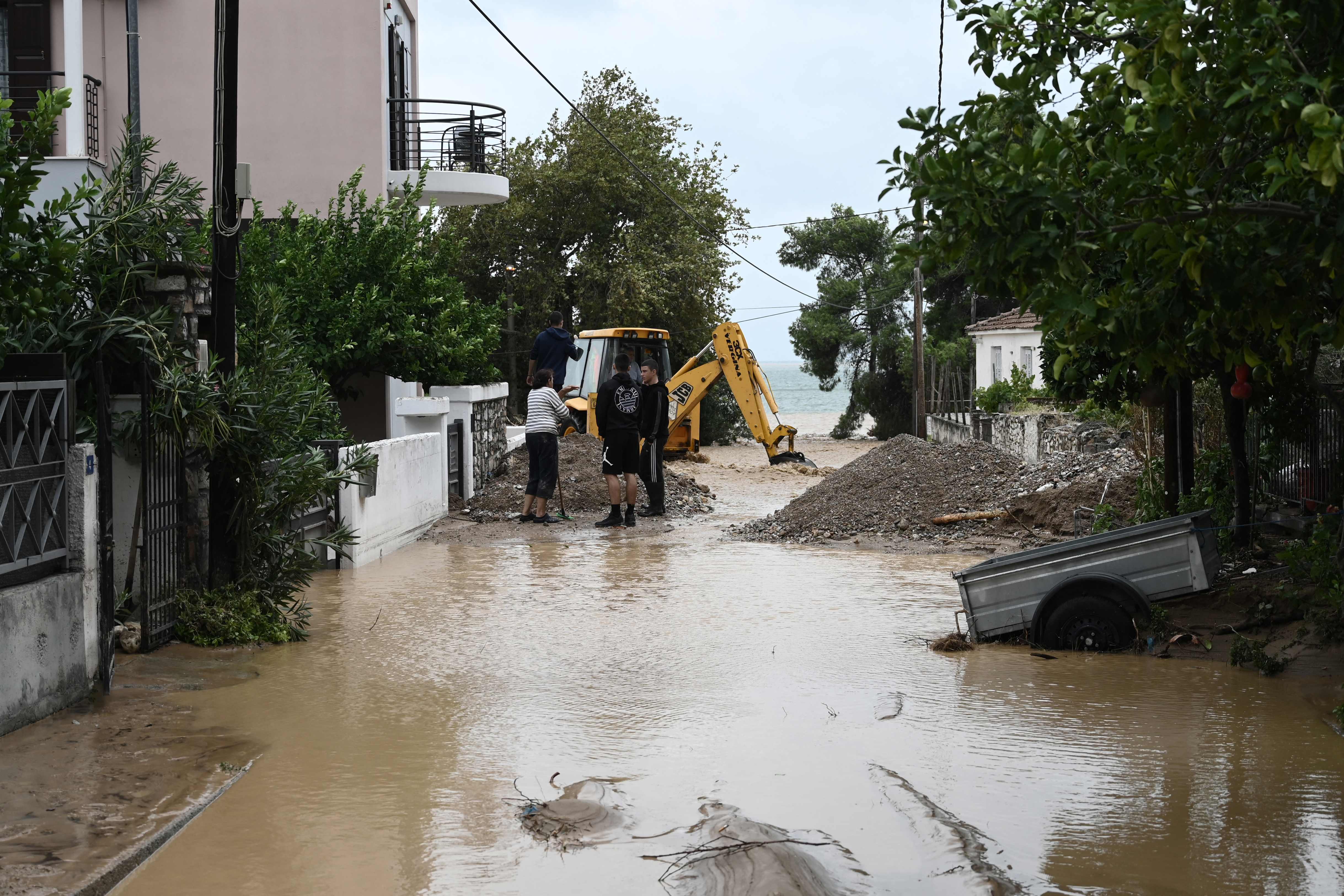 People stand near a digger on a flooded street in Kala Nera near the city of Volos