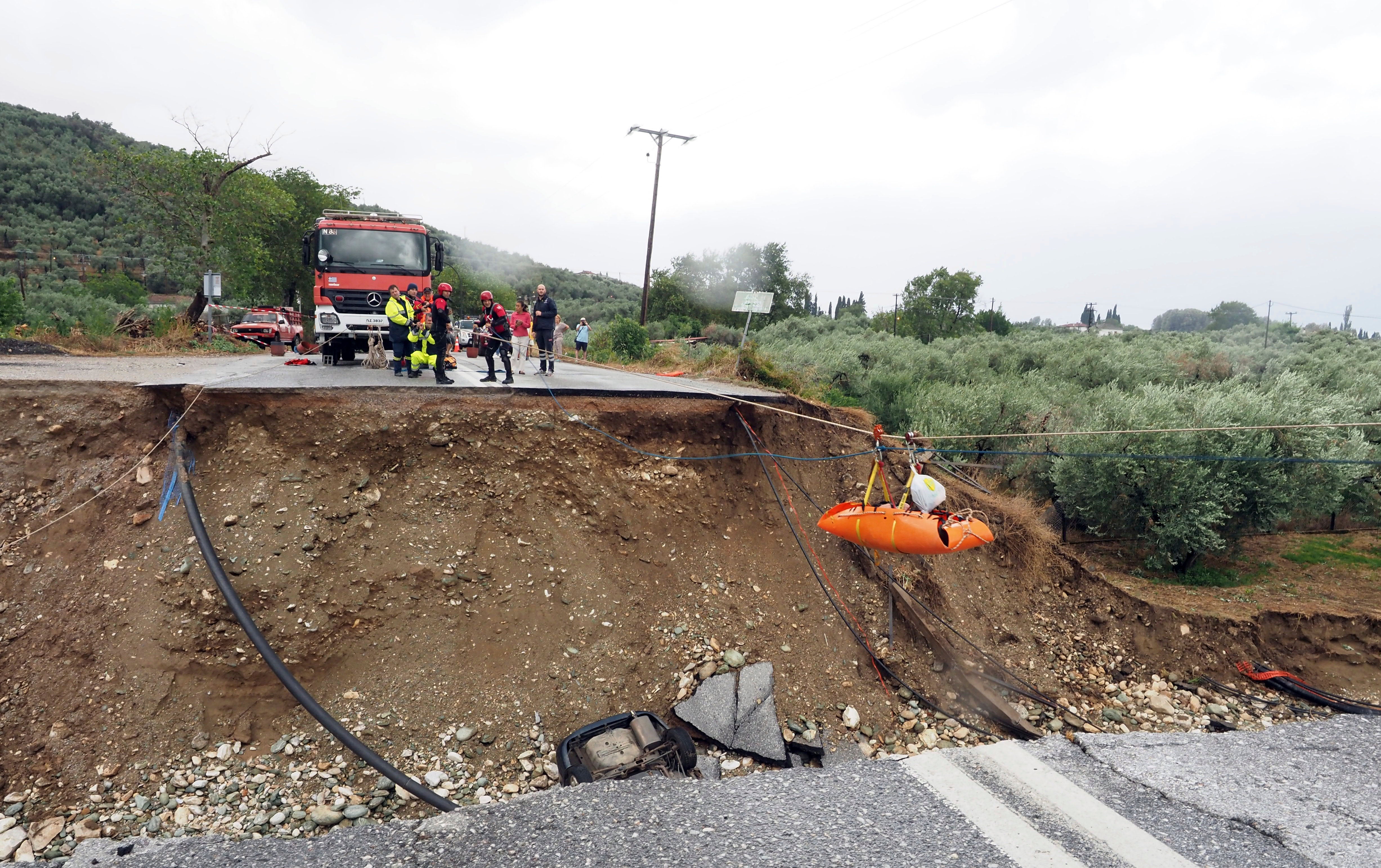 Firefighters use ropes to lift a kidney patient in a stretcher across a road damaged by a rainstorm in Kala Nera village, near Volos