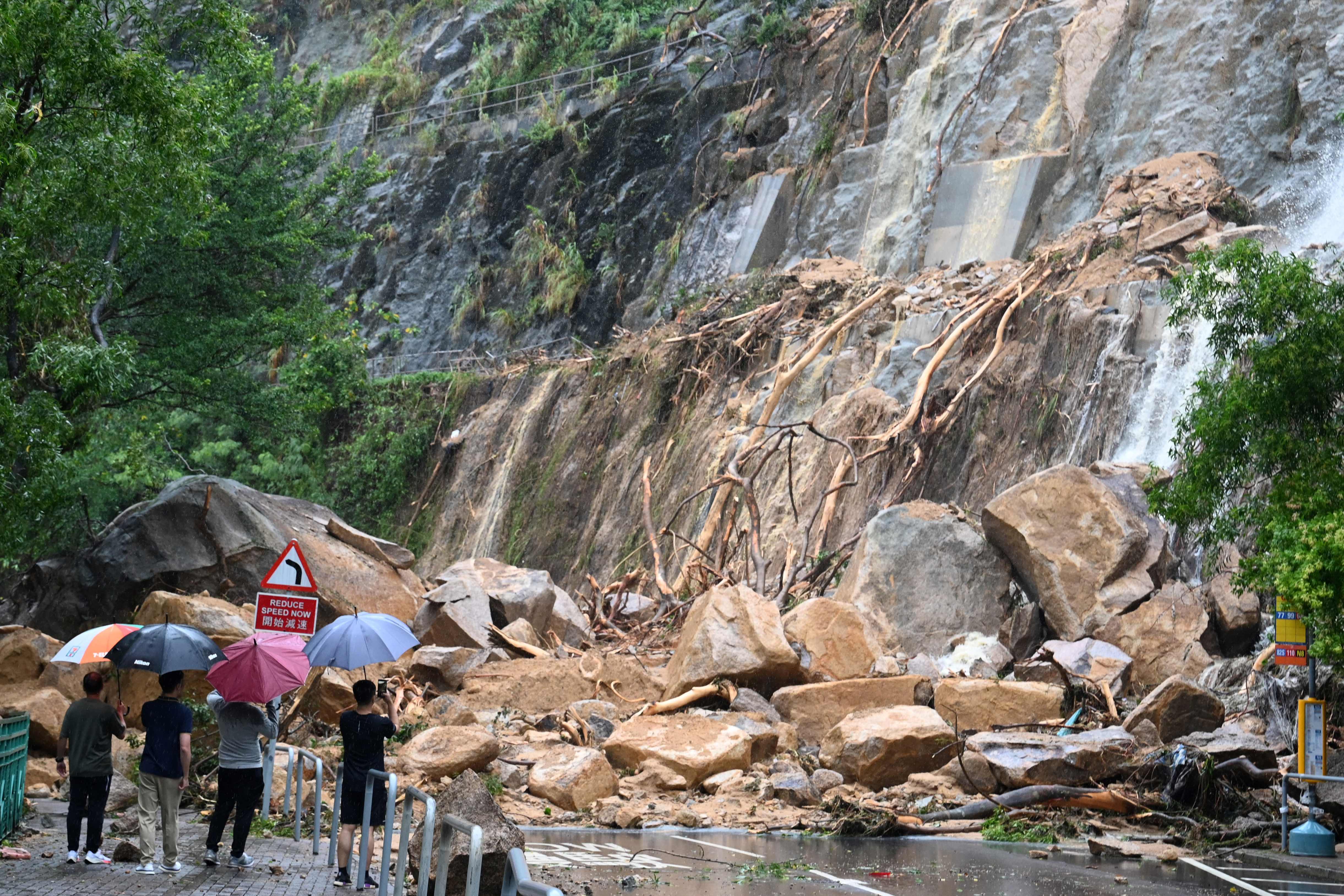 Plainclothes officials and police look at a landslide covering a road at Yiu Tung Estate in Shau Kei Wan in Hong Kong