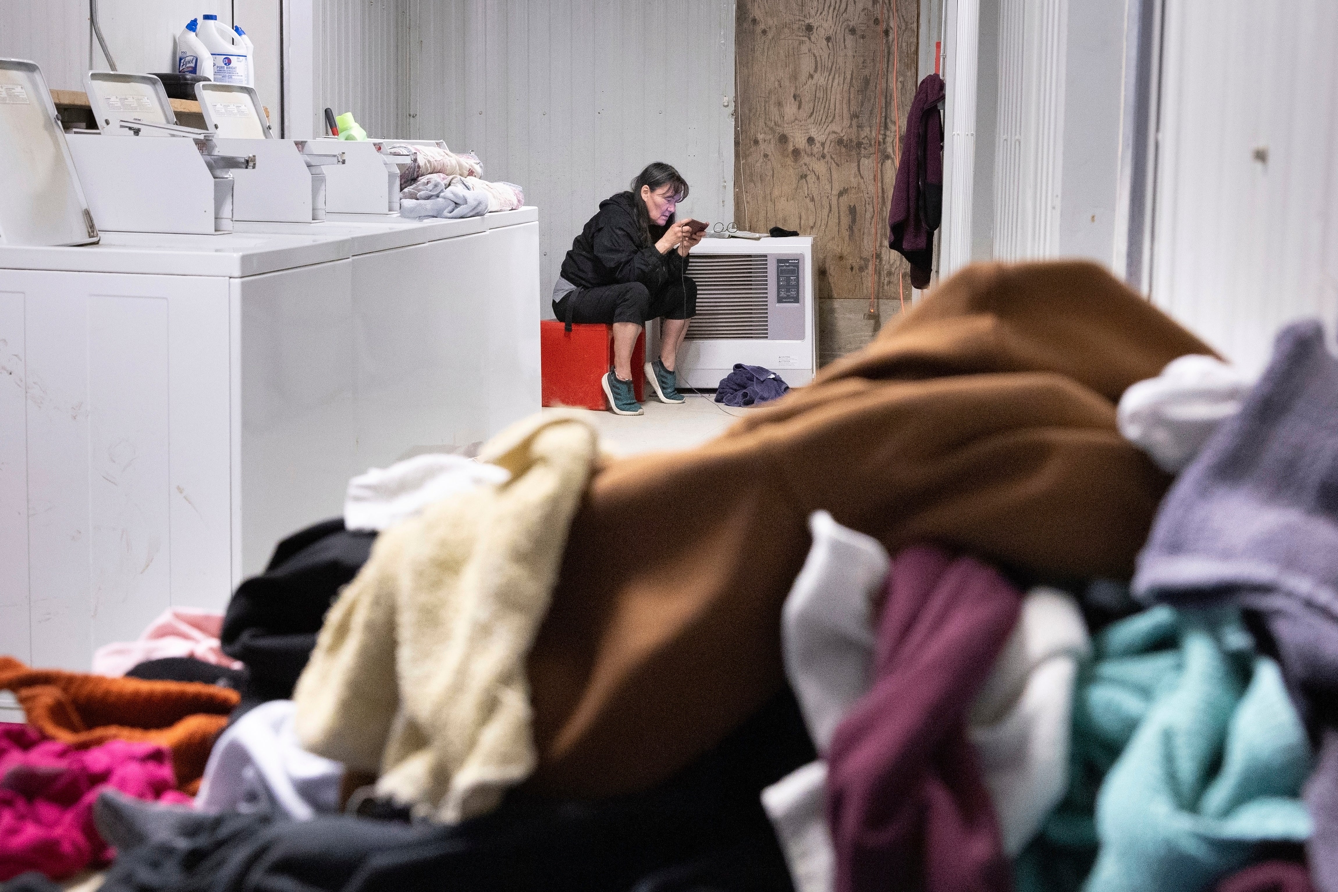 File: A woman uses a cell phone while keeping watch over washing machine
