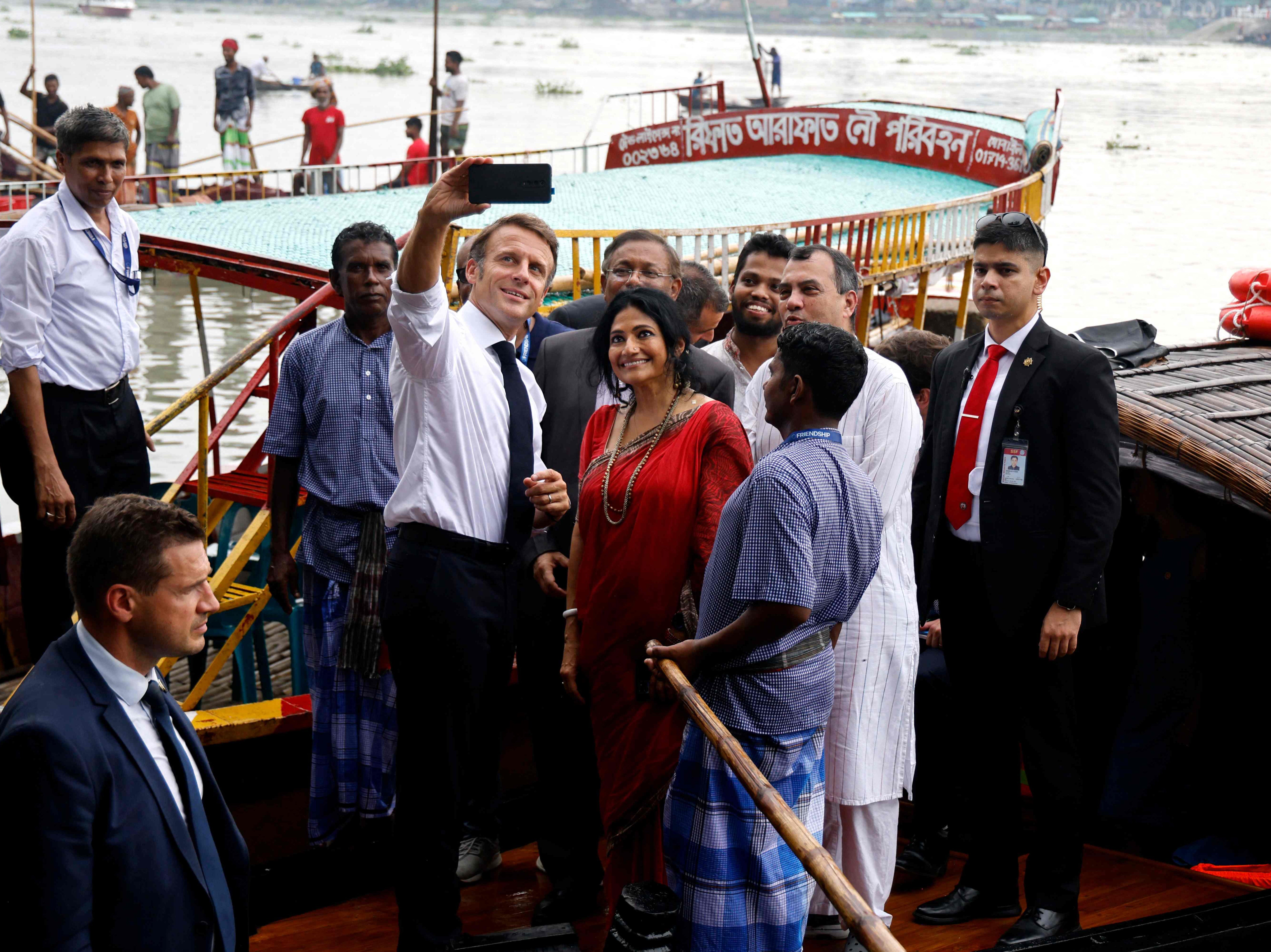 France’s President Emmanuel Macron (C) takes a selfie with Bangladeshi locals and members of an NGO after a boat ride during his two-day visit in Dhaka