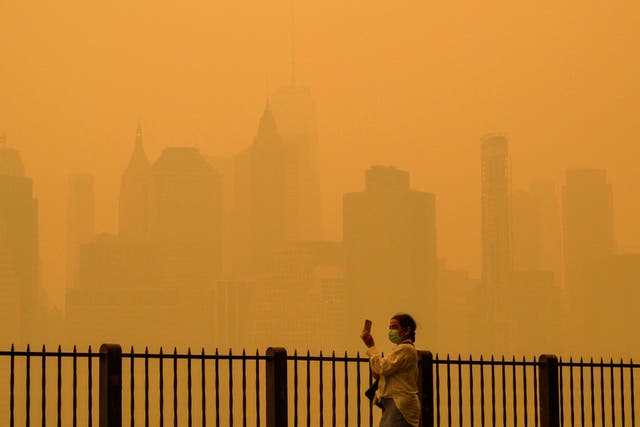 <p>A person wearing a face mask takes photos of the skyline as smoke from wildfires in Canada cause hazy conditions in New York City on June 7, 2023</p>